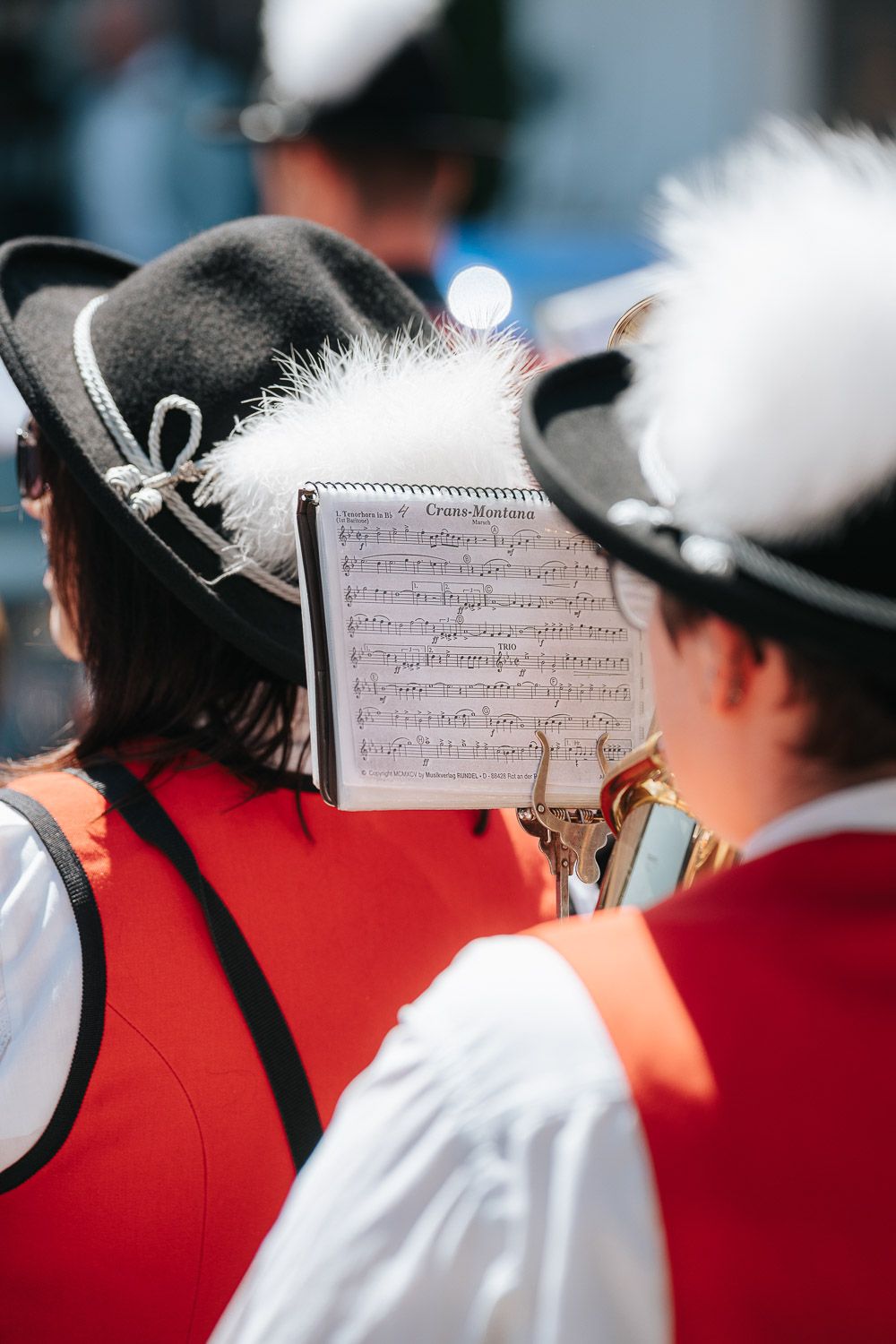 Sheet music displayed on music stands during an outdoor performance by musicians wearing red and white uniforms.