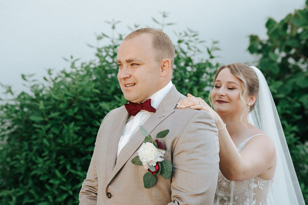 A couple shares a joyful moment during their outdoor wedding ceremony, with the bride in a veil and groom in beige suit.