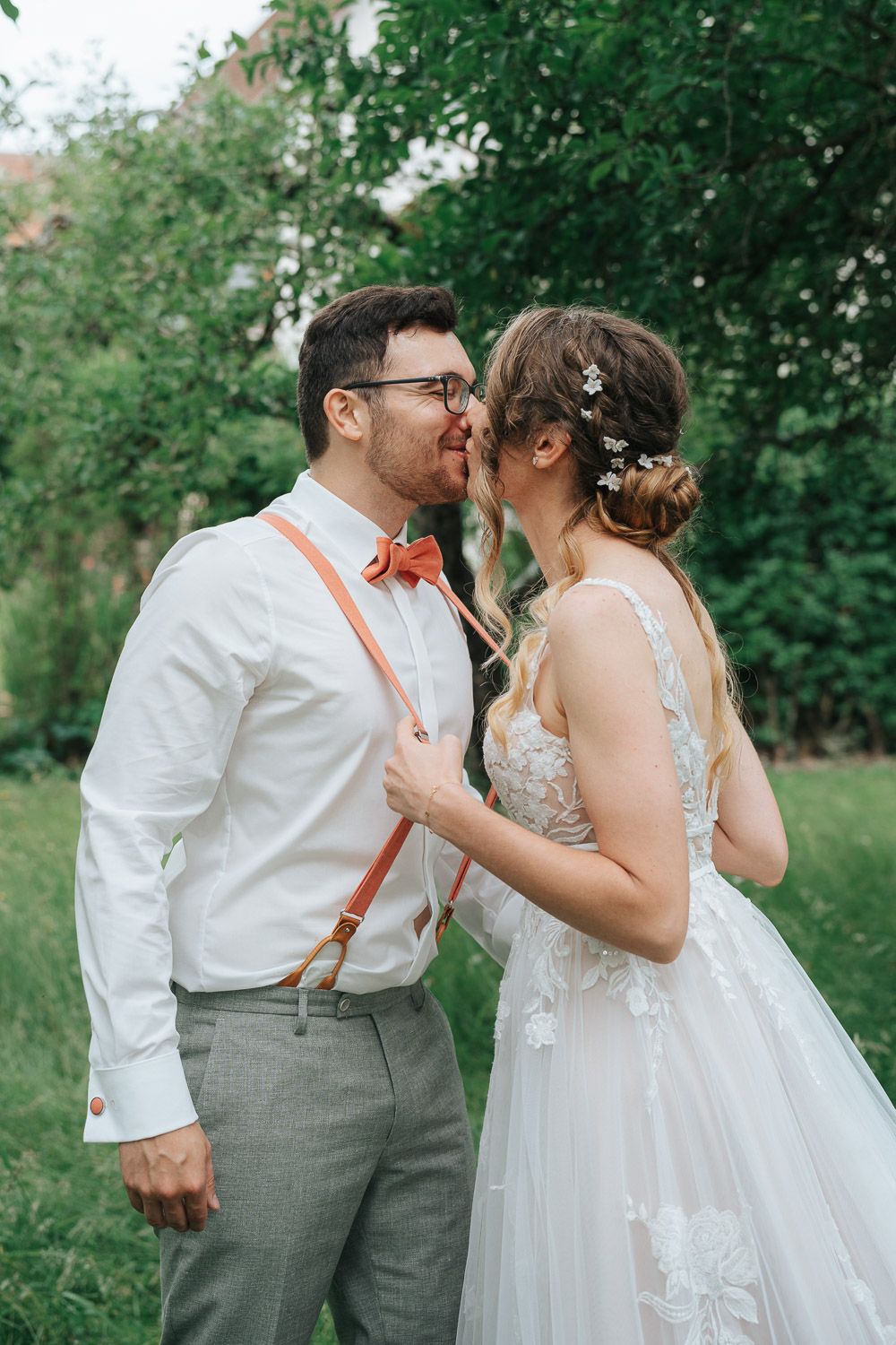 A romantic moment captured in a garden setting with white lace dress and gray suit details.