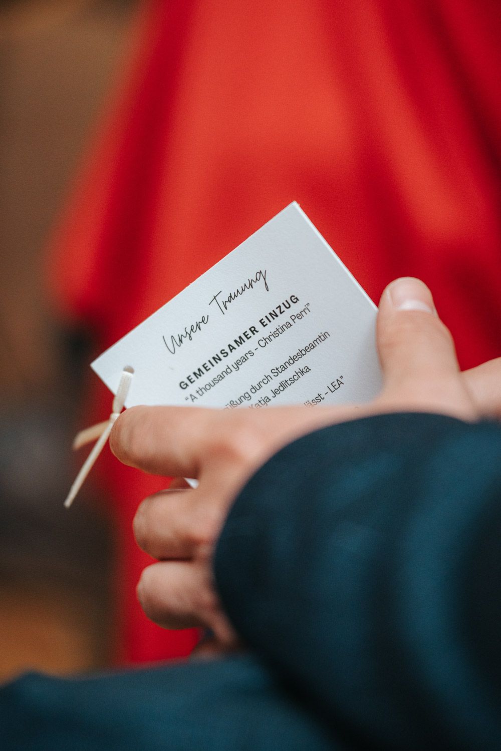 A white business card being held against a blurred red and dark blue background.