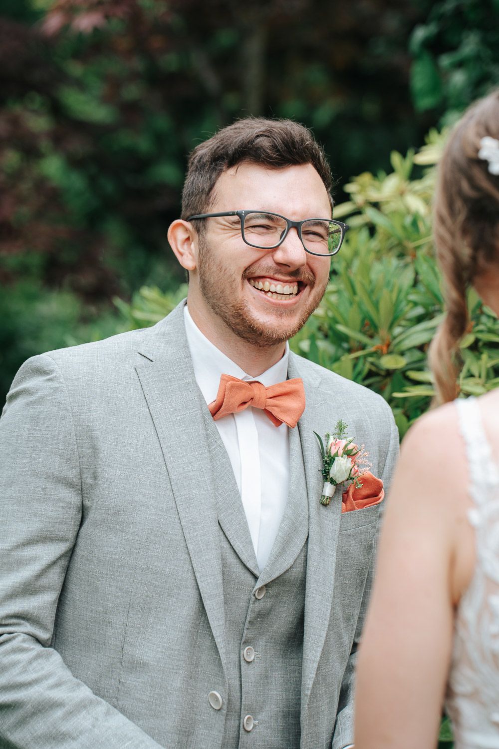 Five candid photos showing someone in a light gray suit and coral bowtie smiling at an outdoor wedding event.