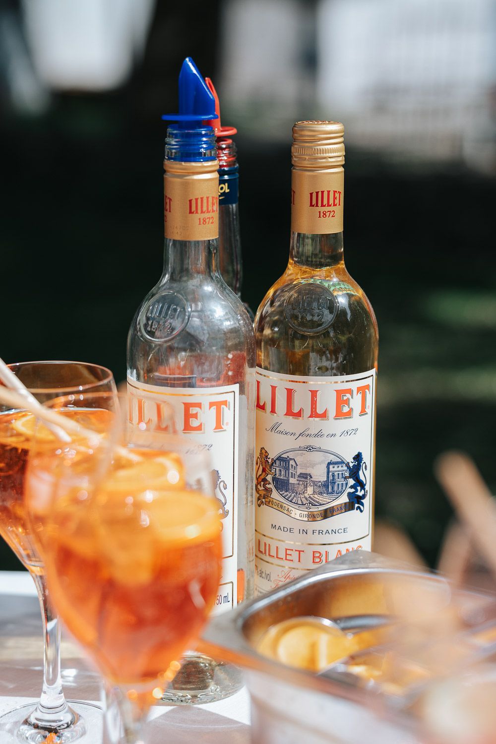 Orange cocktails served in glasses with Lillet vermouth bottles in the background at a bar.