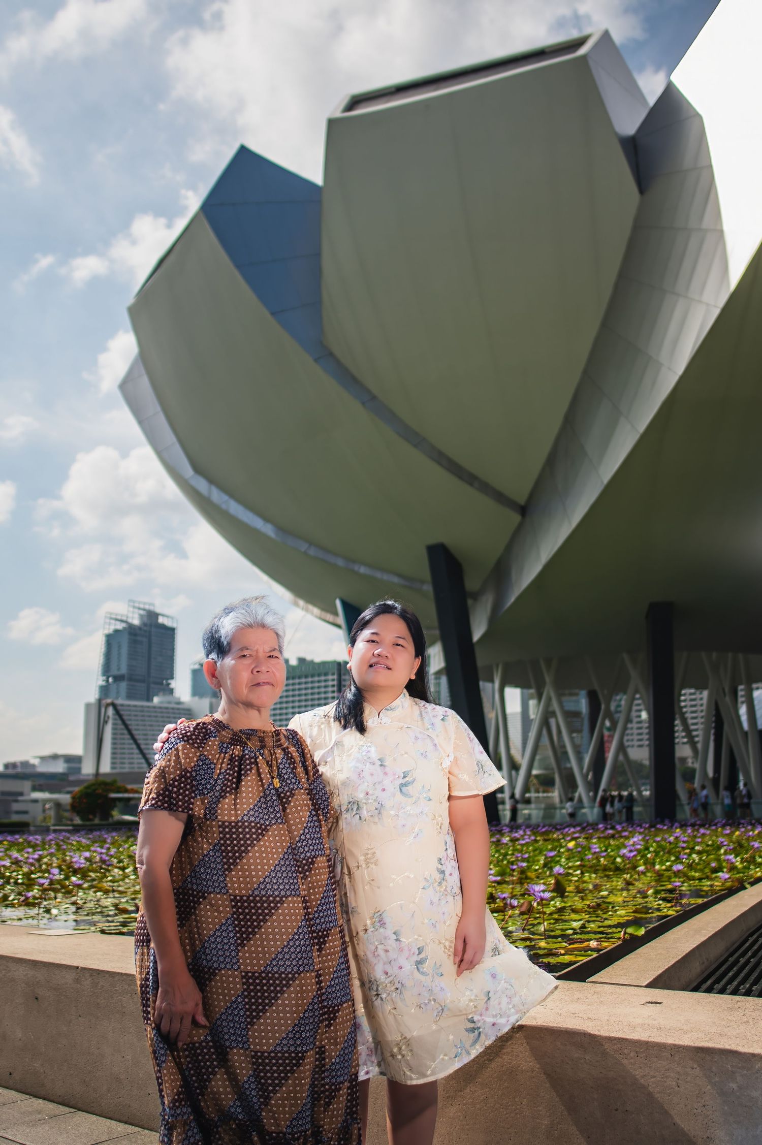 A couple poses in front of modern architectural structures and a flower garden at ArtScience Museum Singapore.