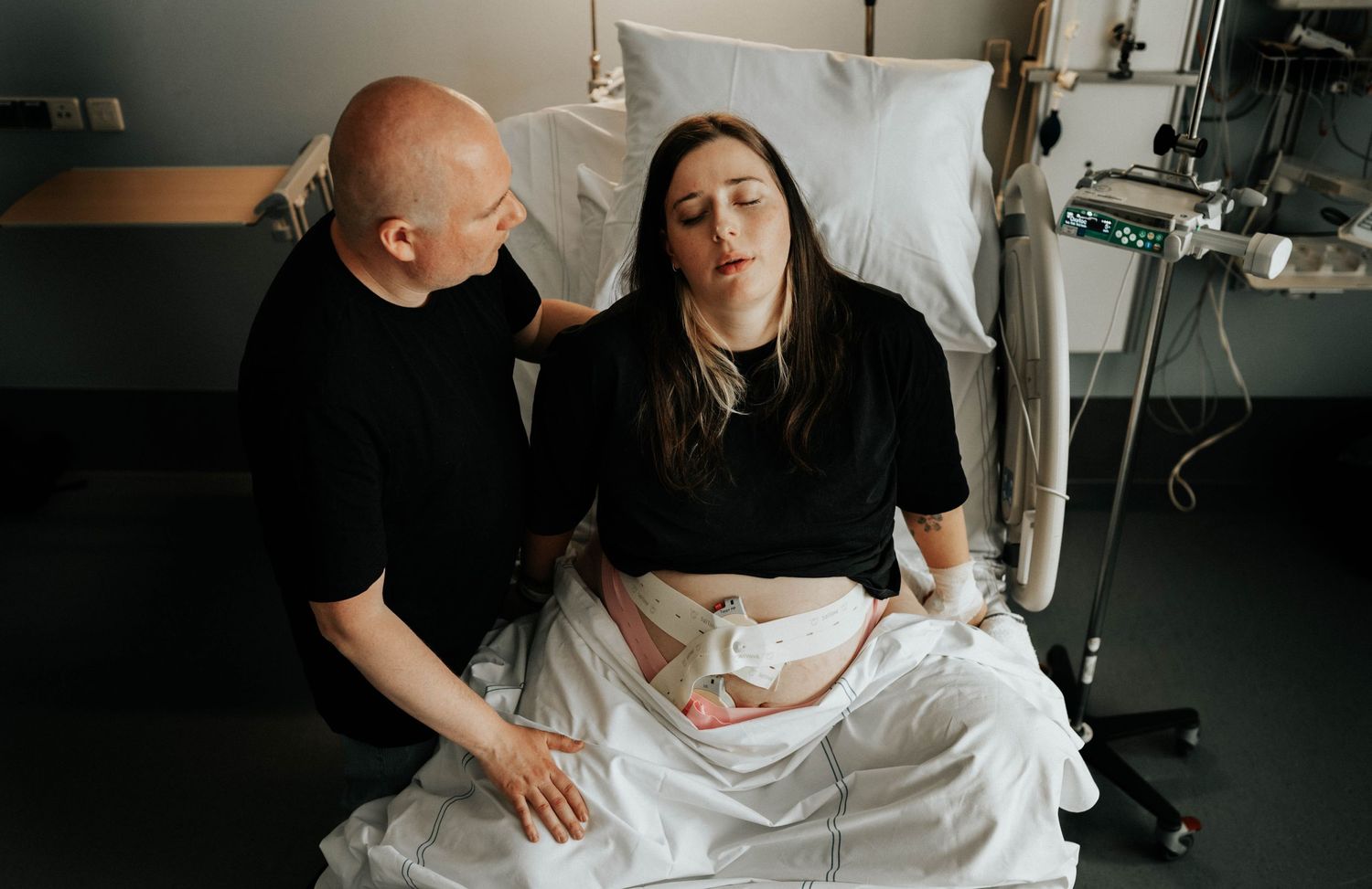 A couple shares an emotional moment during labor in a dimly lit hospital room.