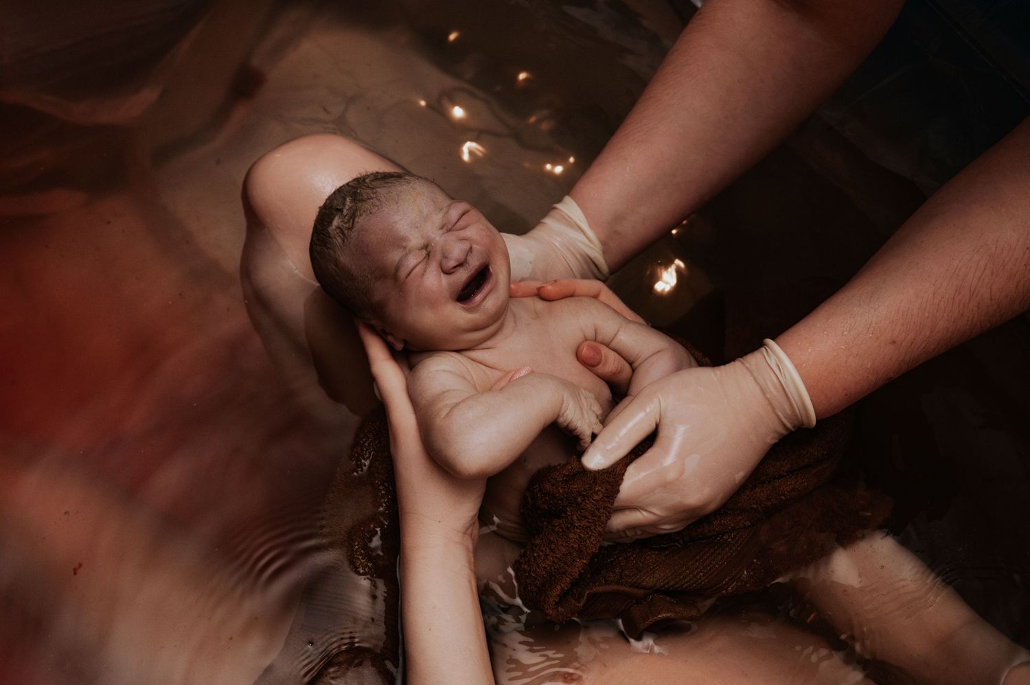 A newborn baby receives calming water therapy during a gentle bath in warm, dimly lit water.