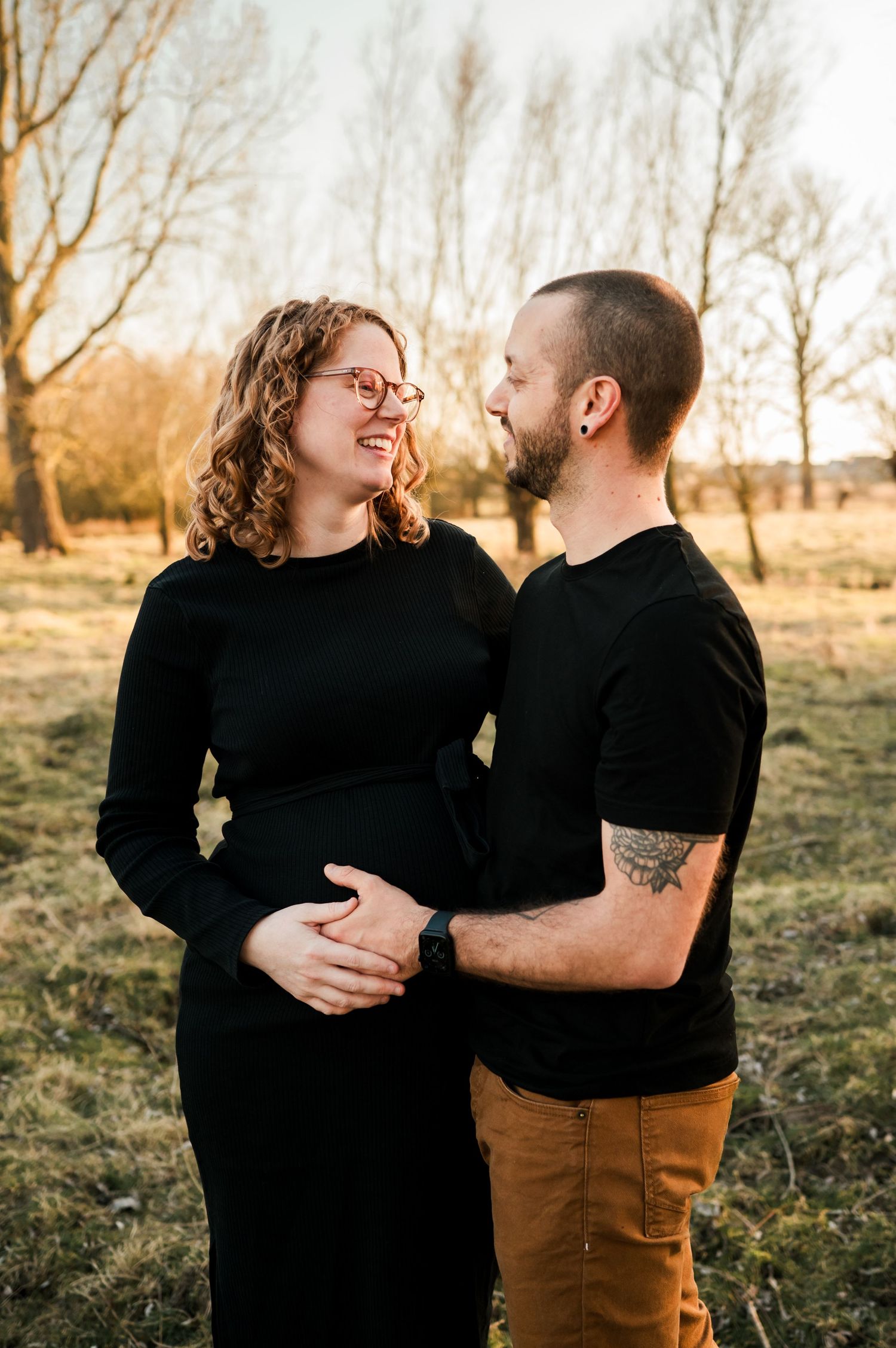 A couple in matching black tops share an intimate moment in a golden autumn field at sunset.
