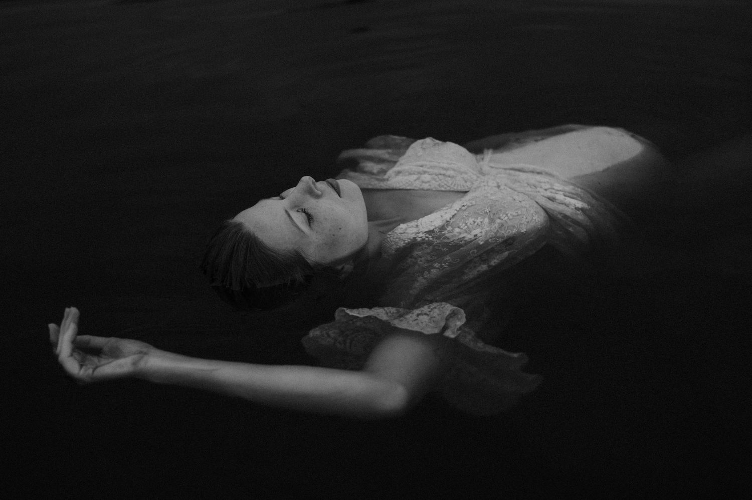 Dramatic black and white underwater photograph showing a floating figure in flowing fabric.