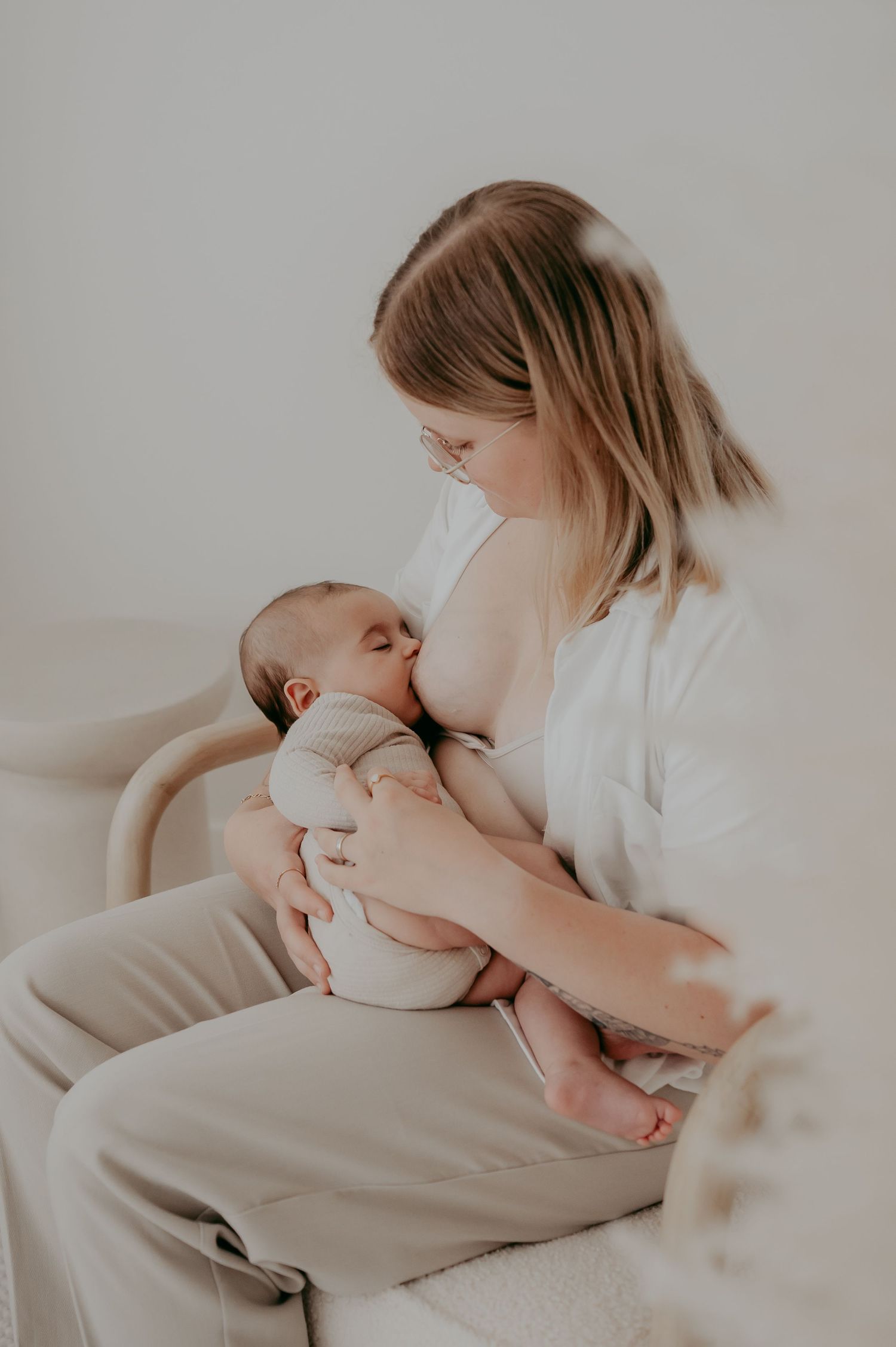 Intimate moment of parent cradling sleeping infant in white clothing on beige chair.