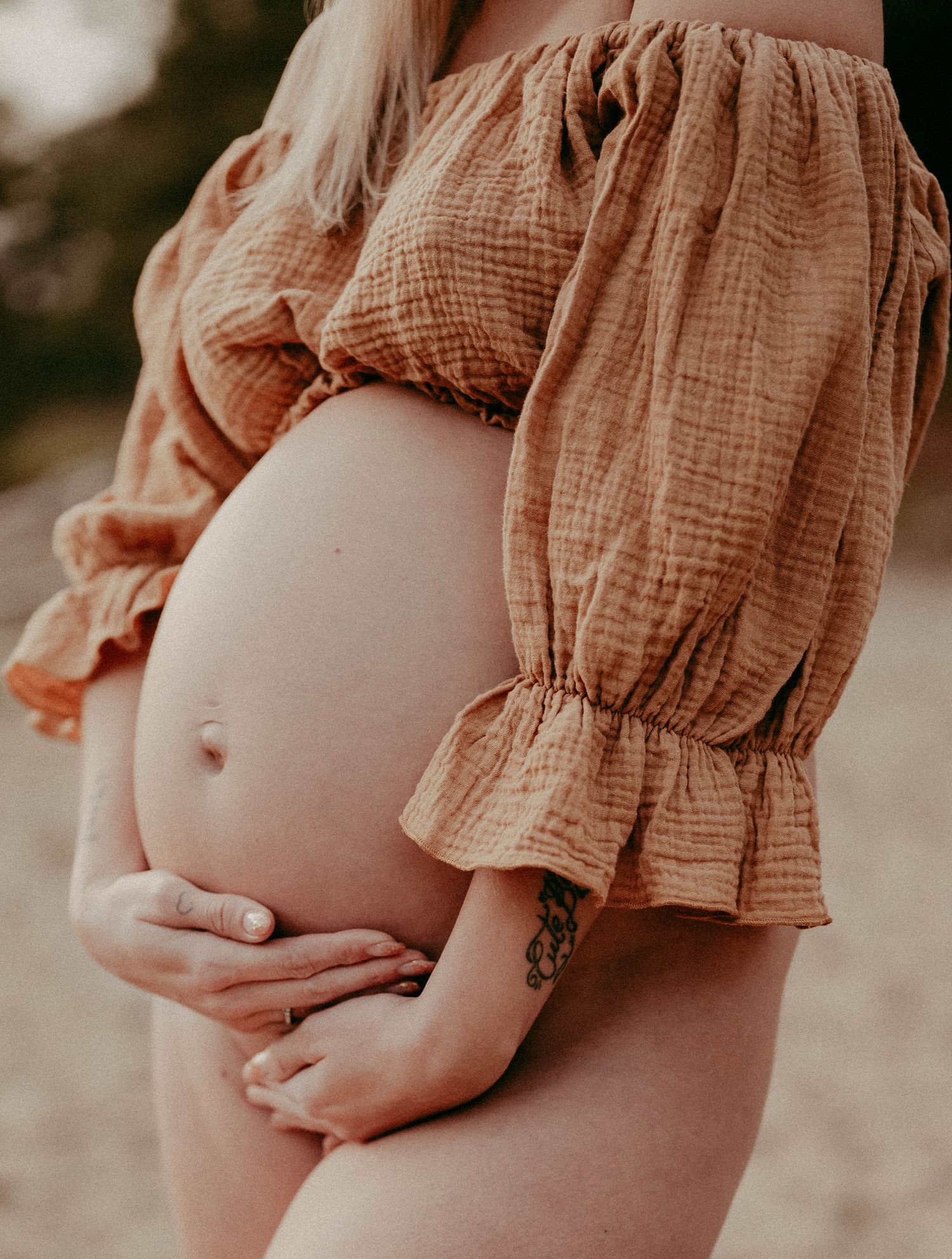 Close-up of pregnant belly with person wearing rustic brown cotton top.