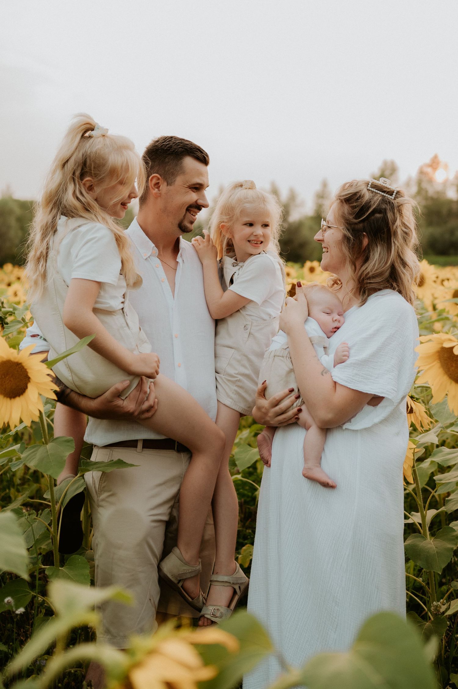 A joyful family portrait in a sunflower field during golden hour wearing coordinated white and beige outfits.
