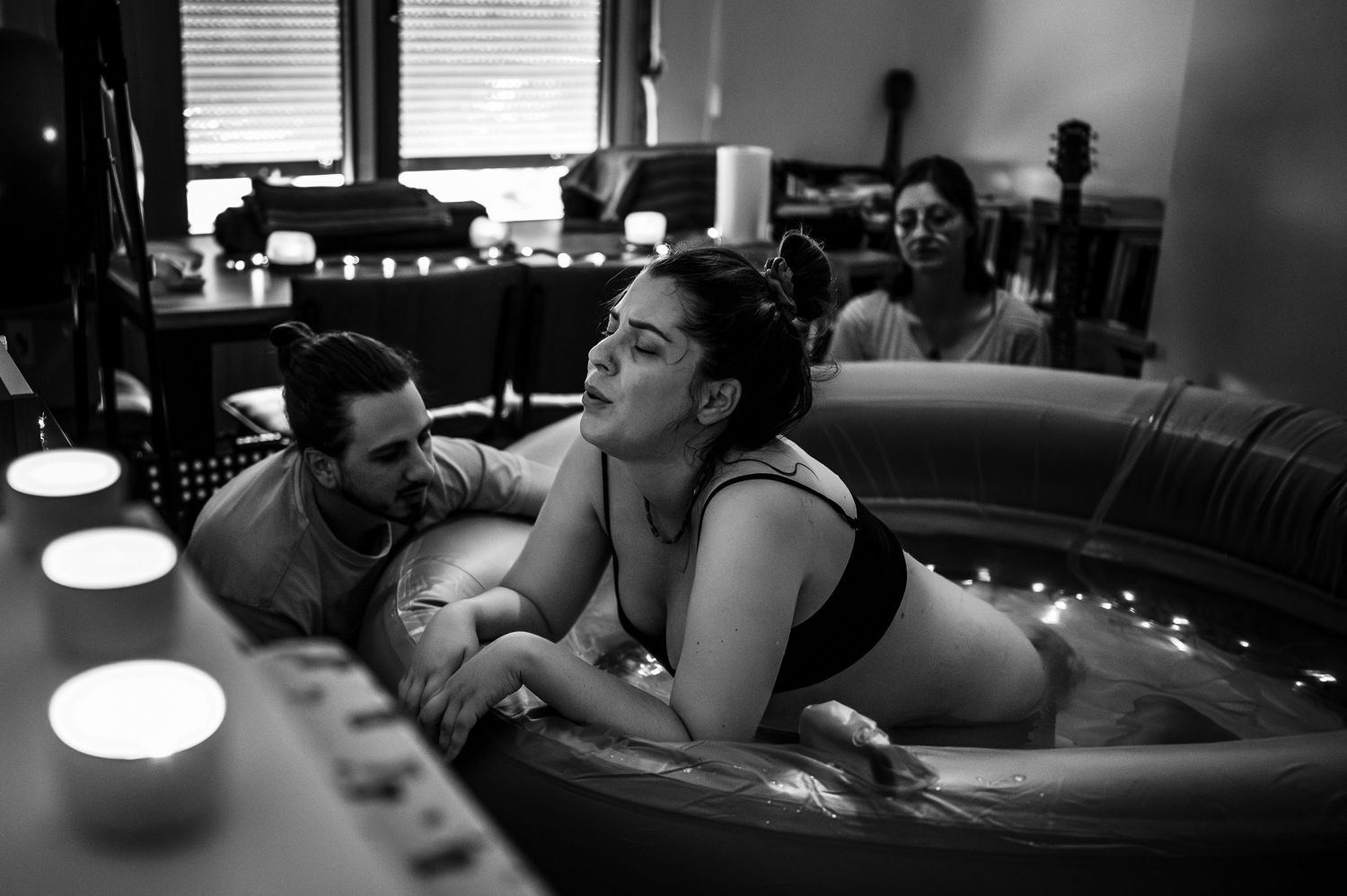 People relax in candlelit hot tub surrounded by soft lighting in black and white photograph.