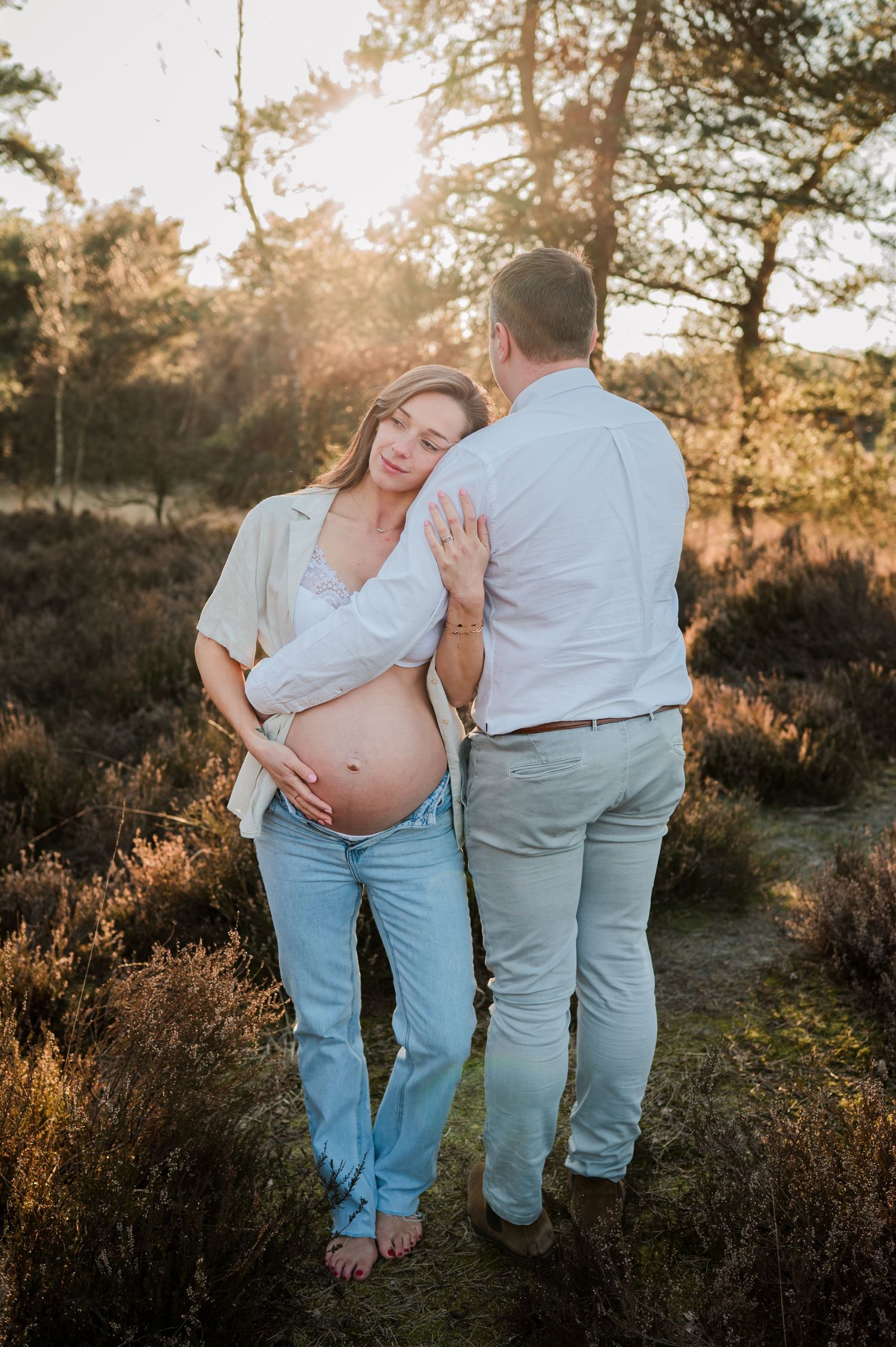 A loving couple shares a tender moment at sunset in a forest setting during a pregnancy photoshoot.