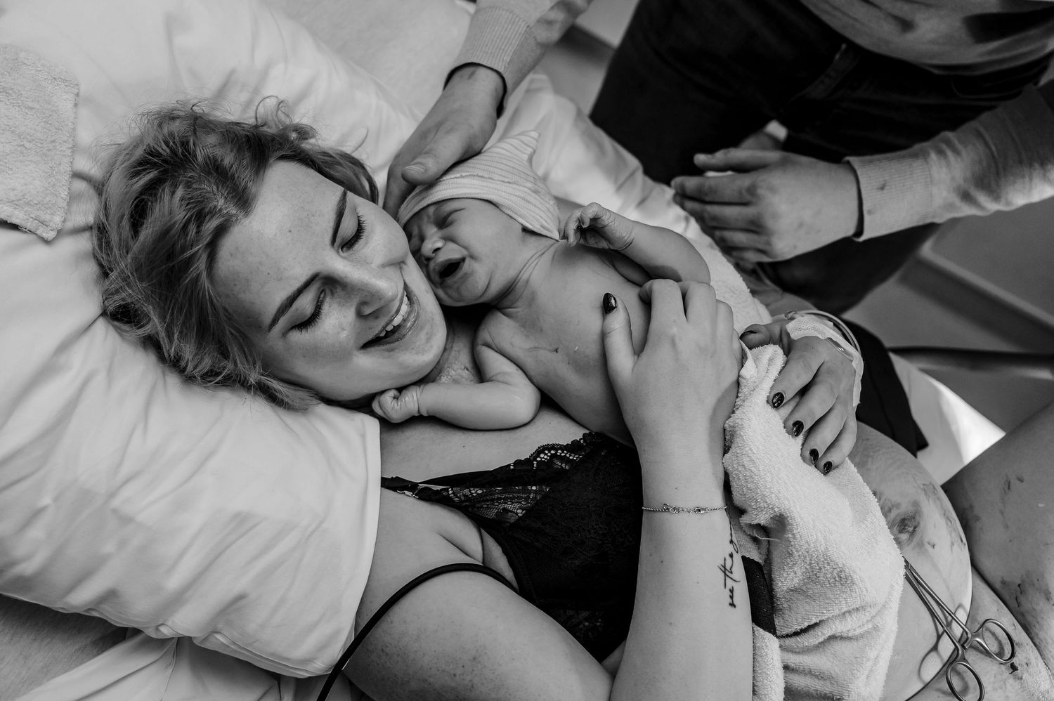 Two people sharing a tender moment of laughter while lying together on white bedding in black and white photography.