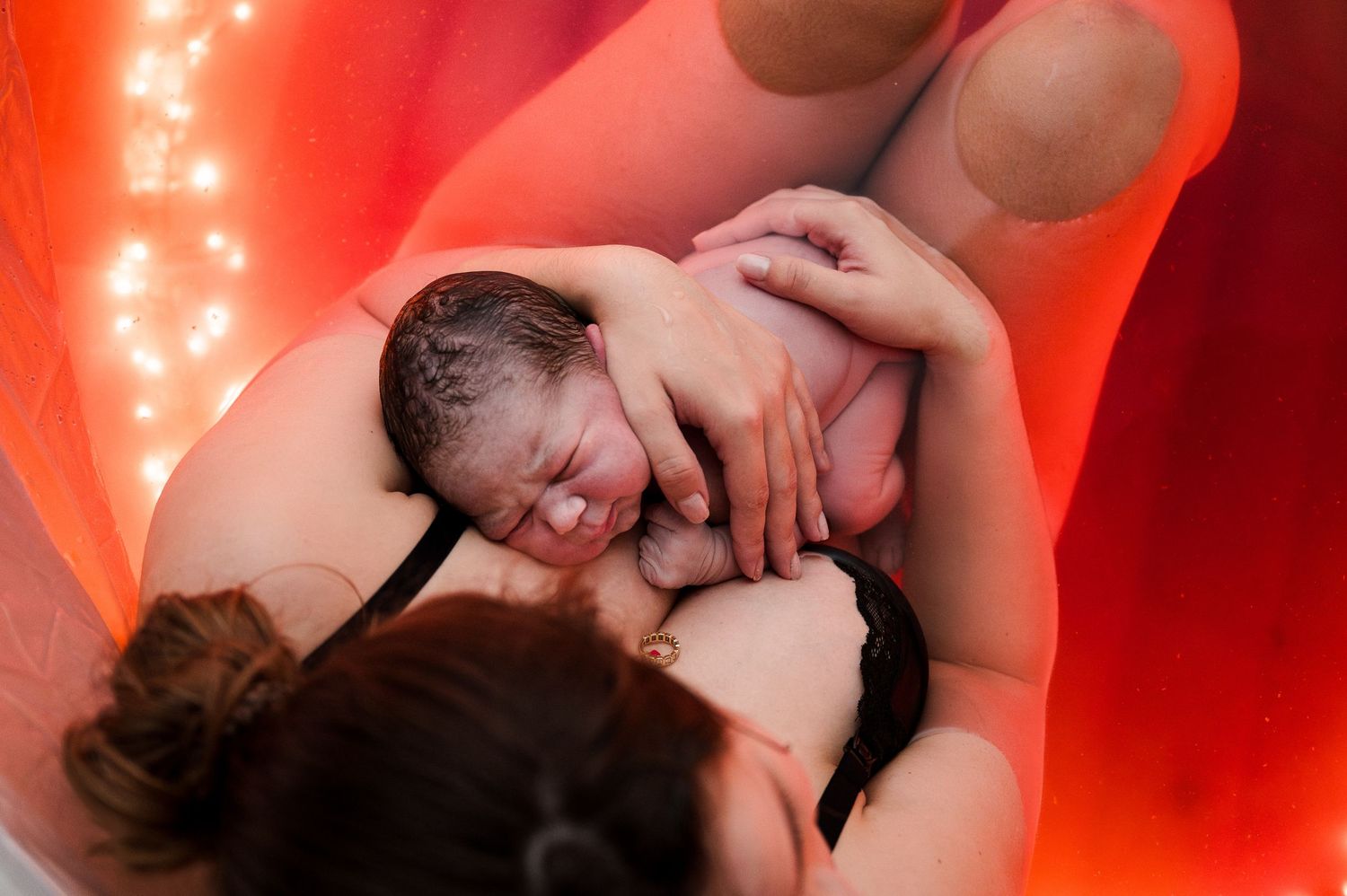 A newborn baby rests on mother's chest moments after birth in a warm, softly lit water birth setting.