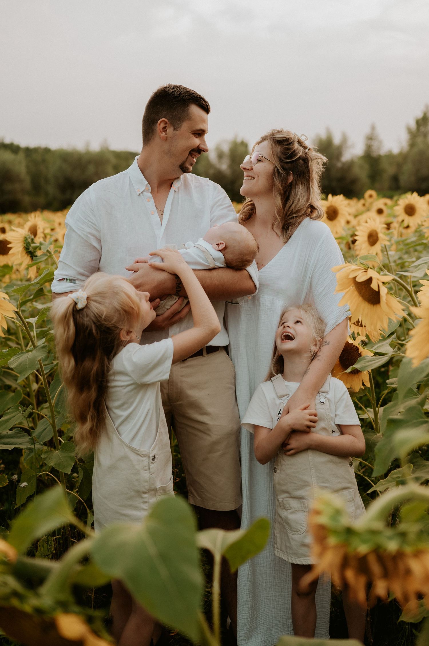 Happy family laughing together in sunflower field at golden hour.