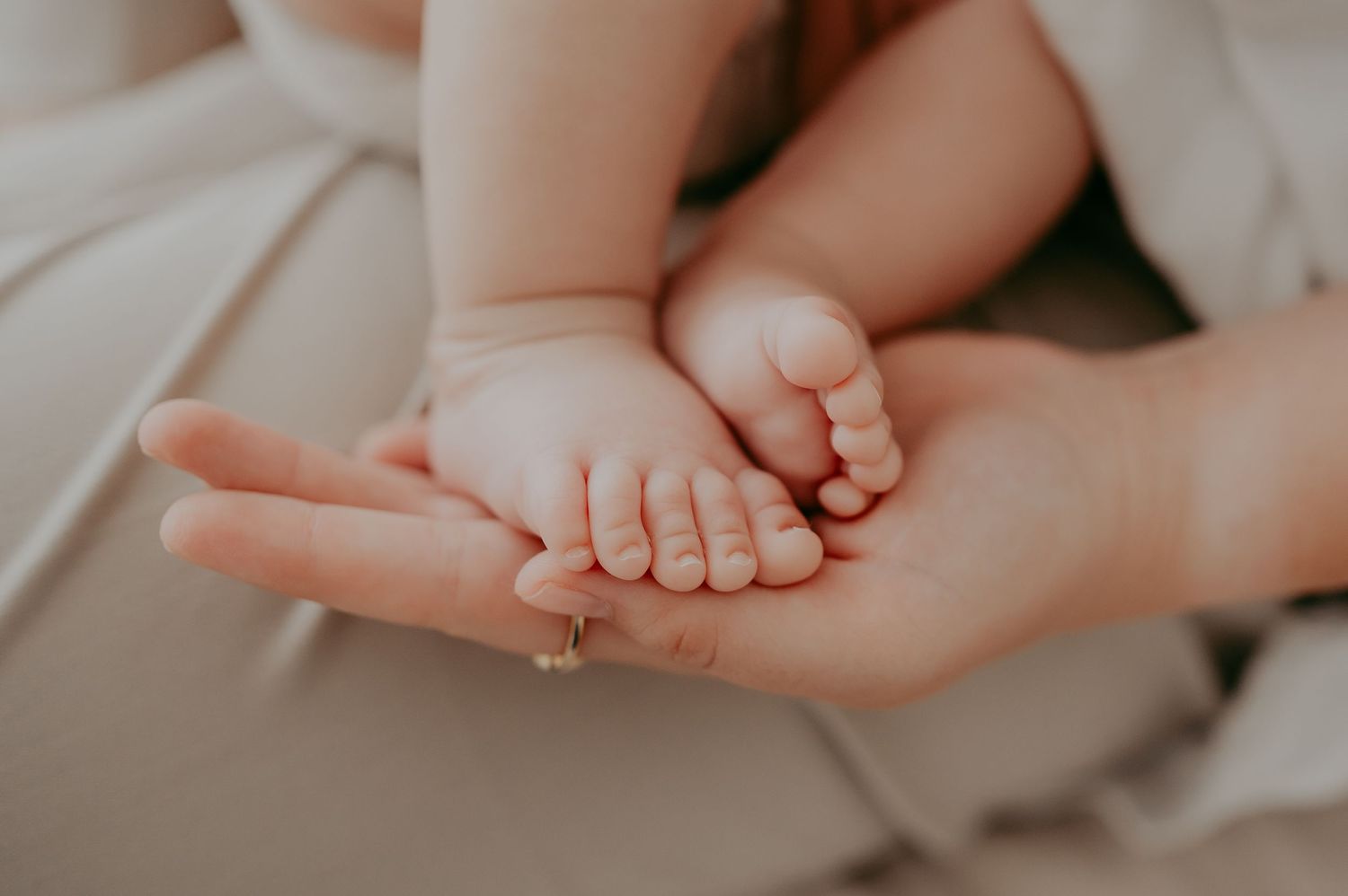 Tiny newborn baby feet resting in gentle hands with a gold ring.