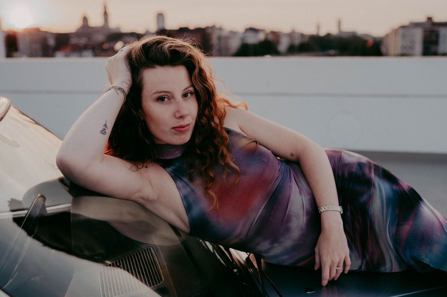 Moody rooftop portrait with urban skyline backdrop and purple dress.