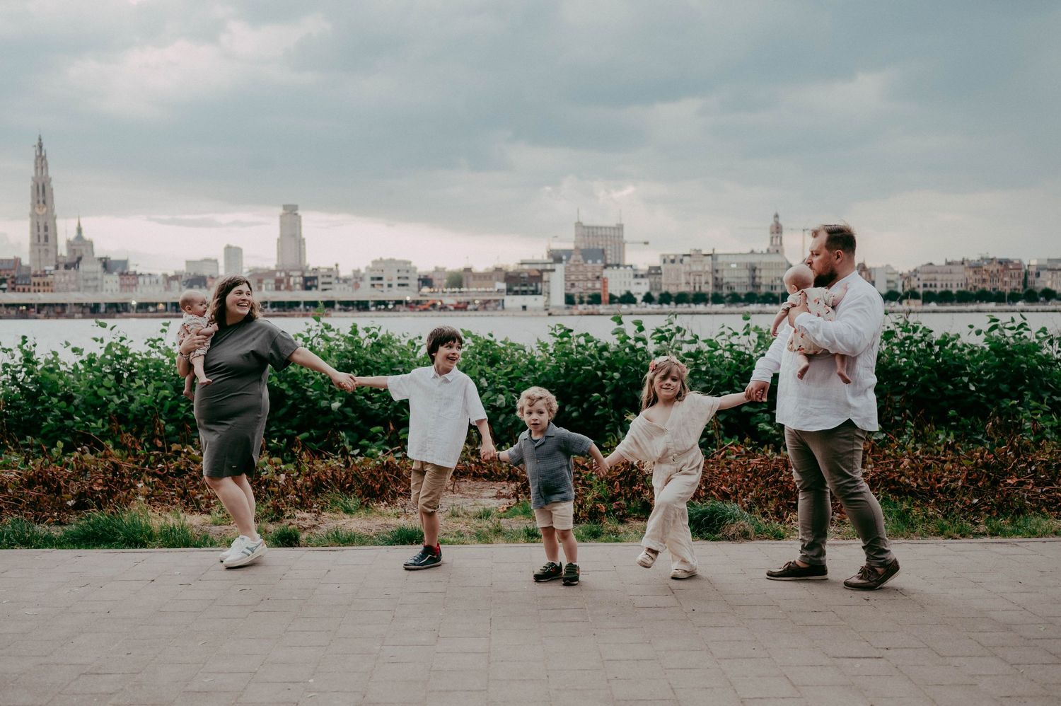 A joyful group dances together on a pathway with a city skyline visible in the background.