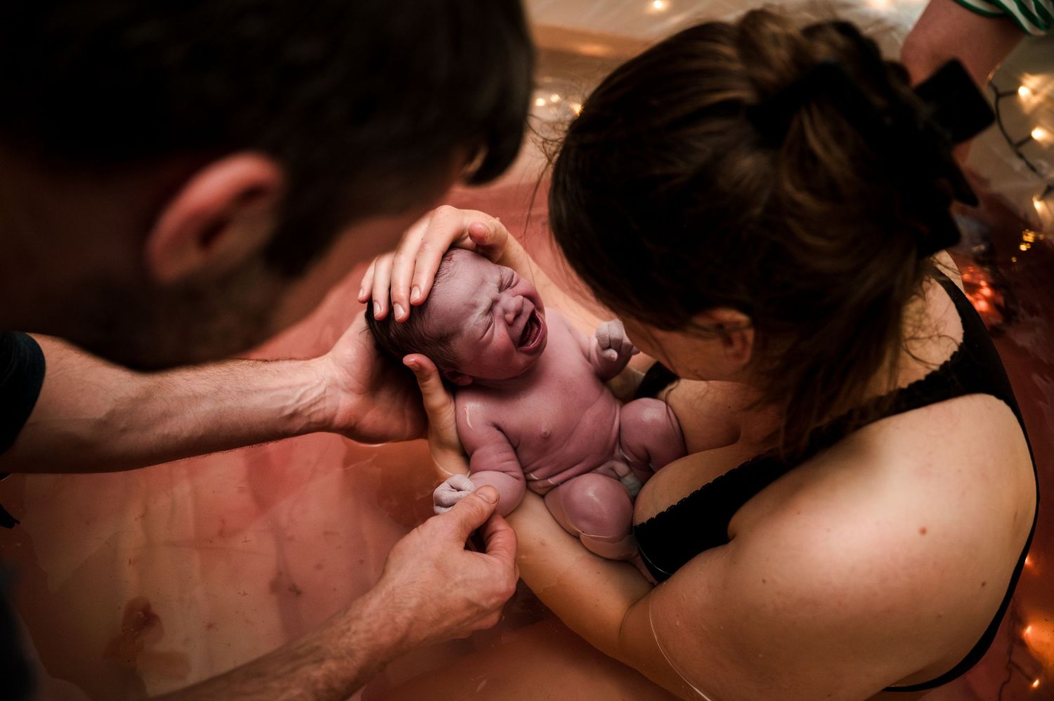 Parents holding their newborn baby moments after birth in an intimate home delivery setting.