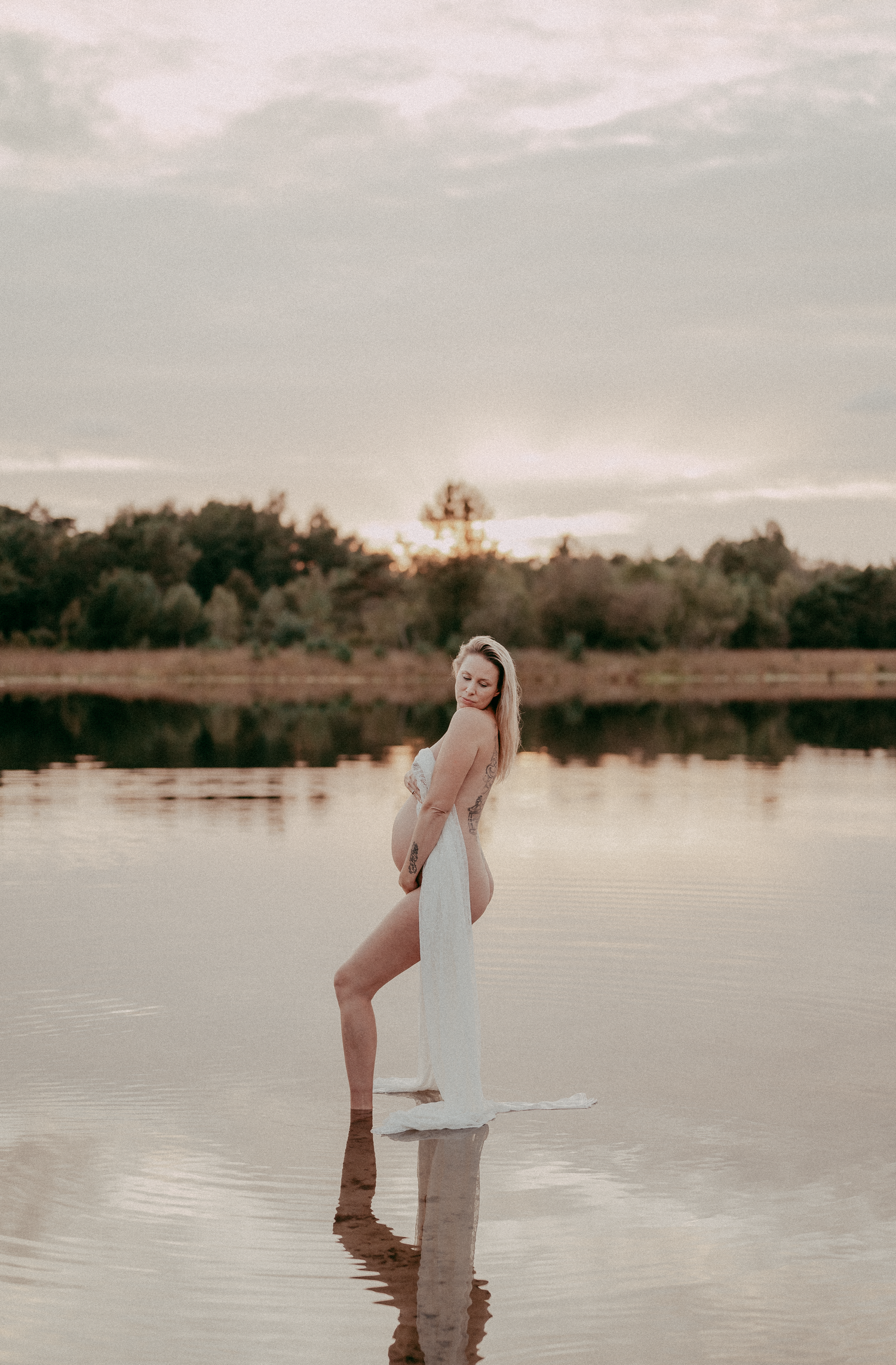 Ethereal maternity portrait at sunset with reflection in still water.