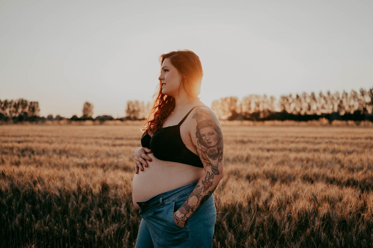 Sunset maternity photo in a wheat field with dramatic golden lighting.