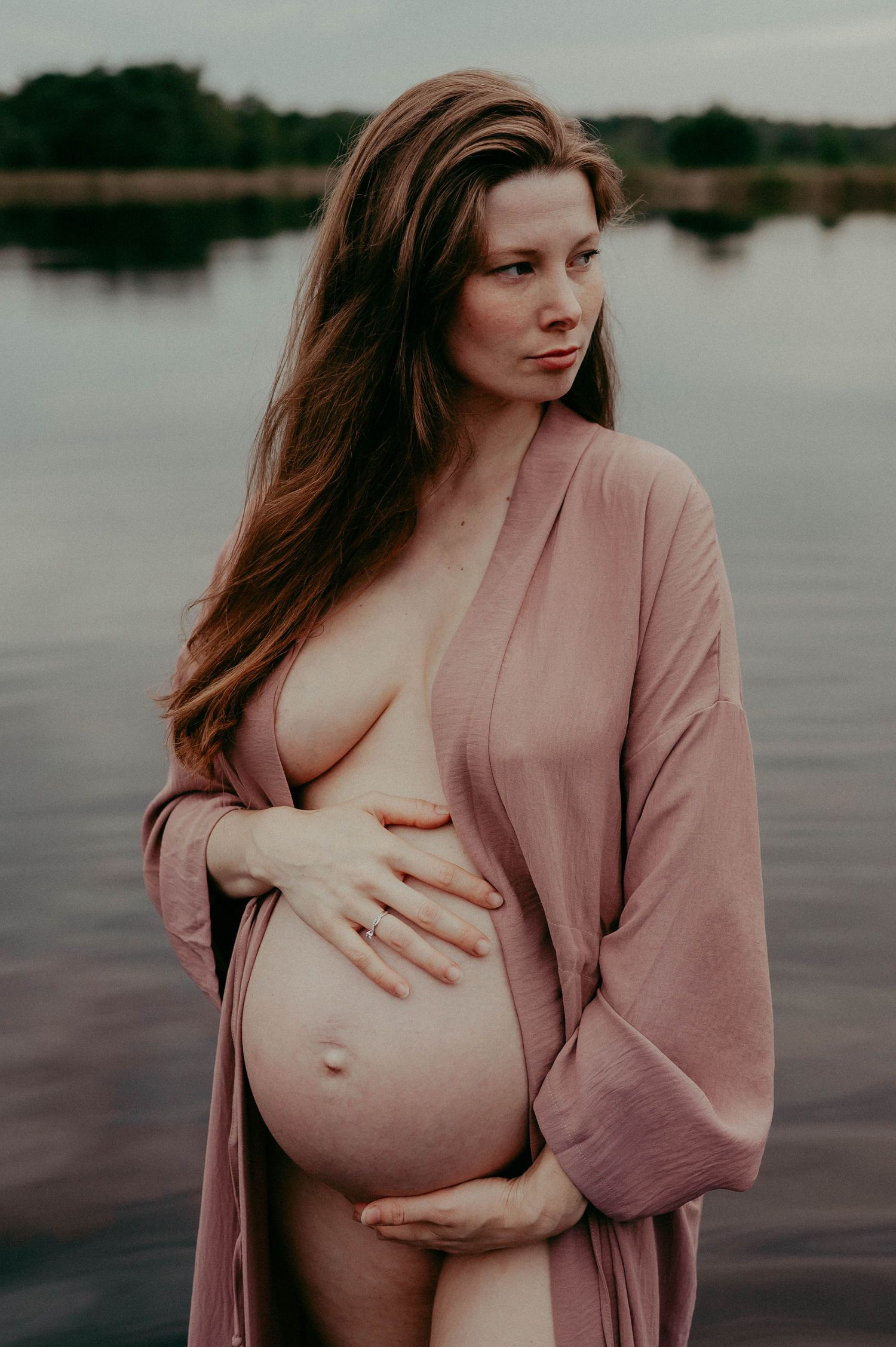 Intimate maternity portrait by a lake featuring an expectant mother in a pink robe.