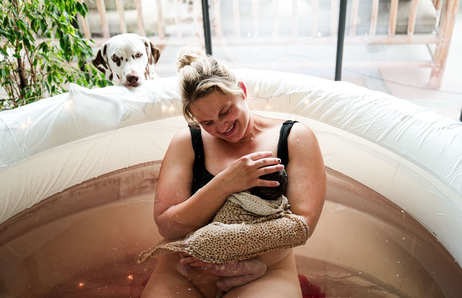 Person relaxing and checking phone while sitting in a brown inflatable pool with a pet dog nearby.