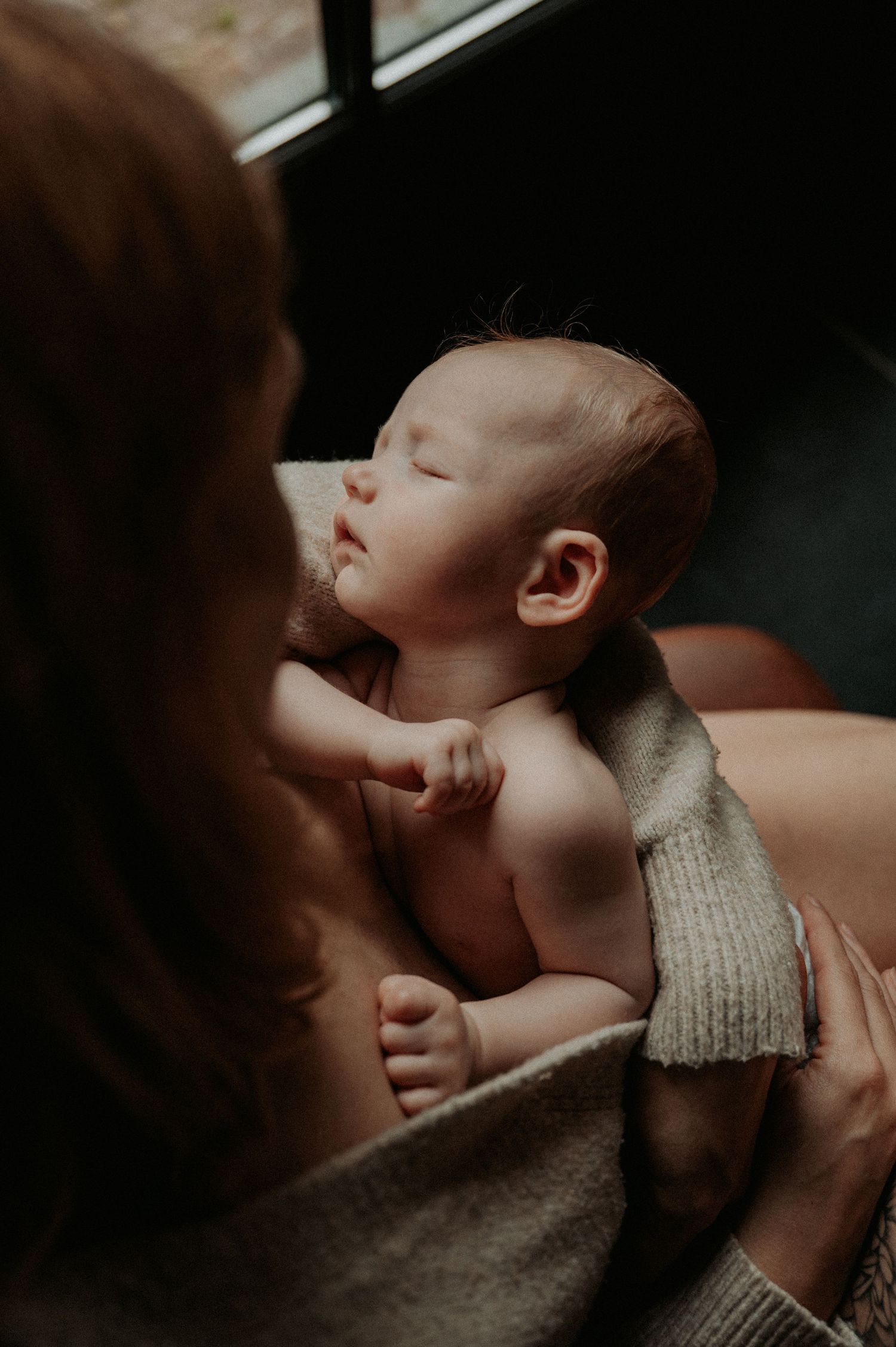 A tender moment between parent and infant in soft, moody lighting.