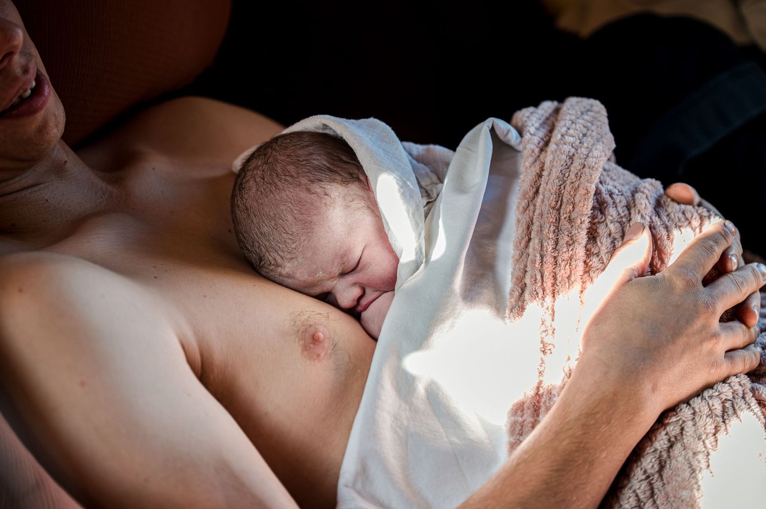 Mother breastfeeding newborn baby in warm natural lighting with soft textiles in view.