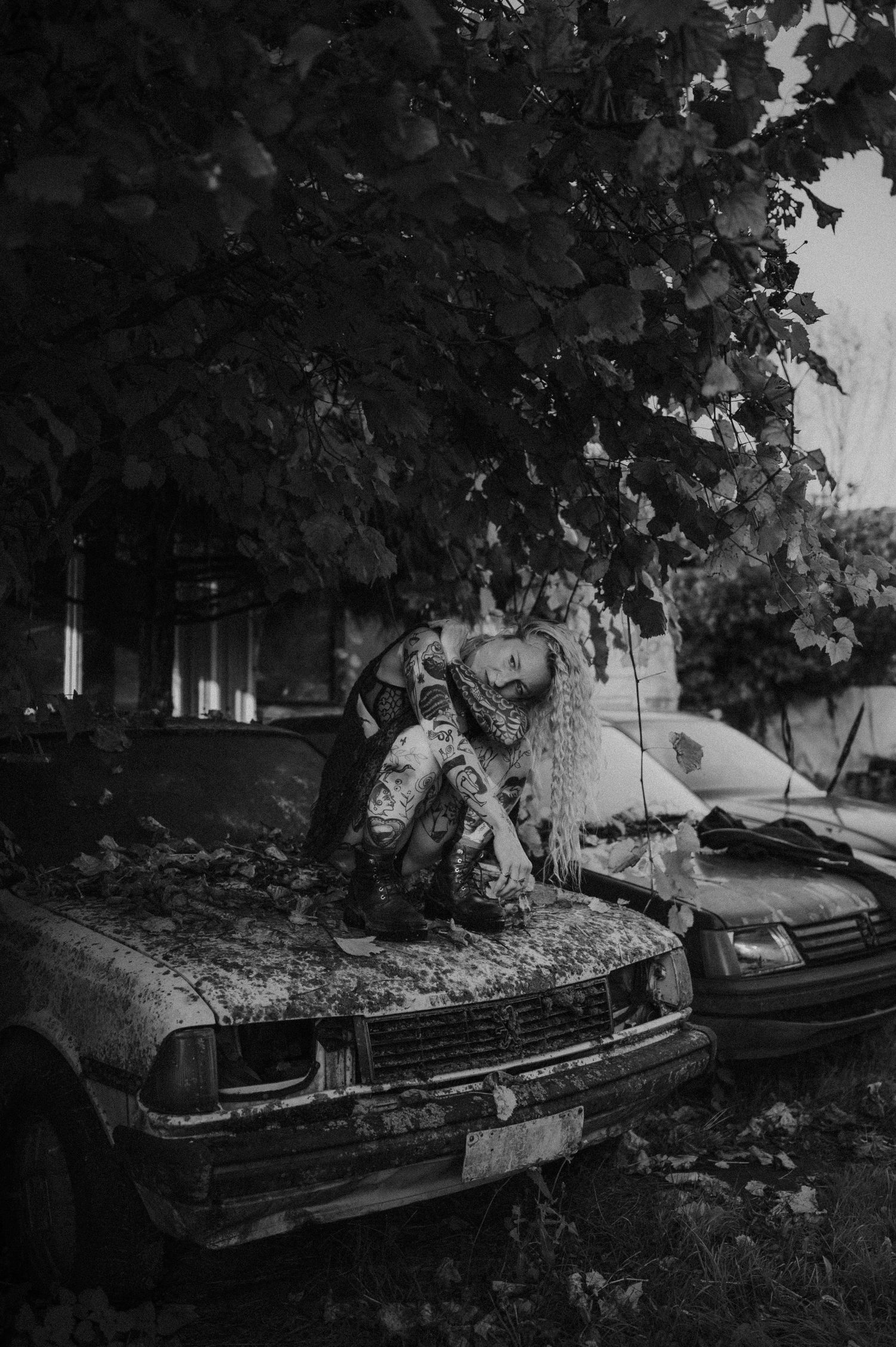 Black and white photo of an old abandoned car covered in leaves.