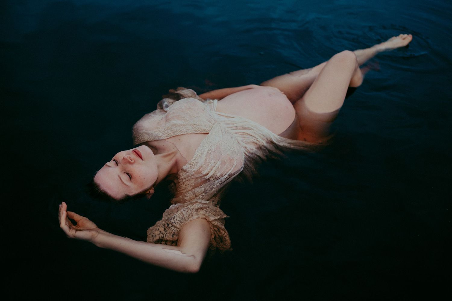 Artistic underwater portrait featuring a floating figure in a light colored dress against dark water.
