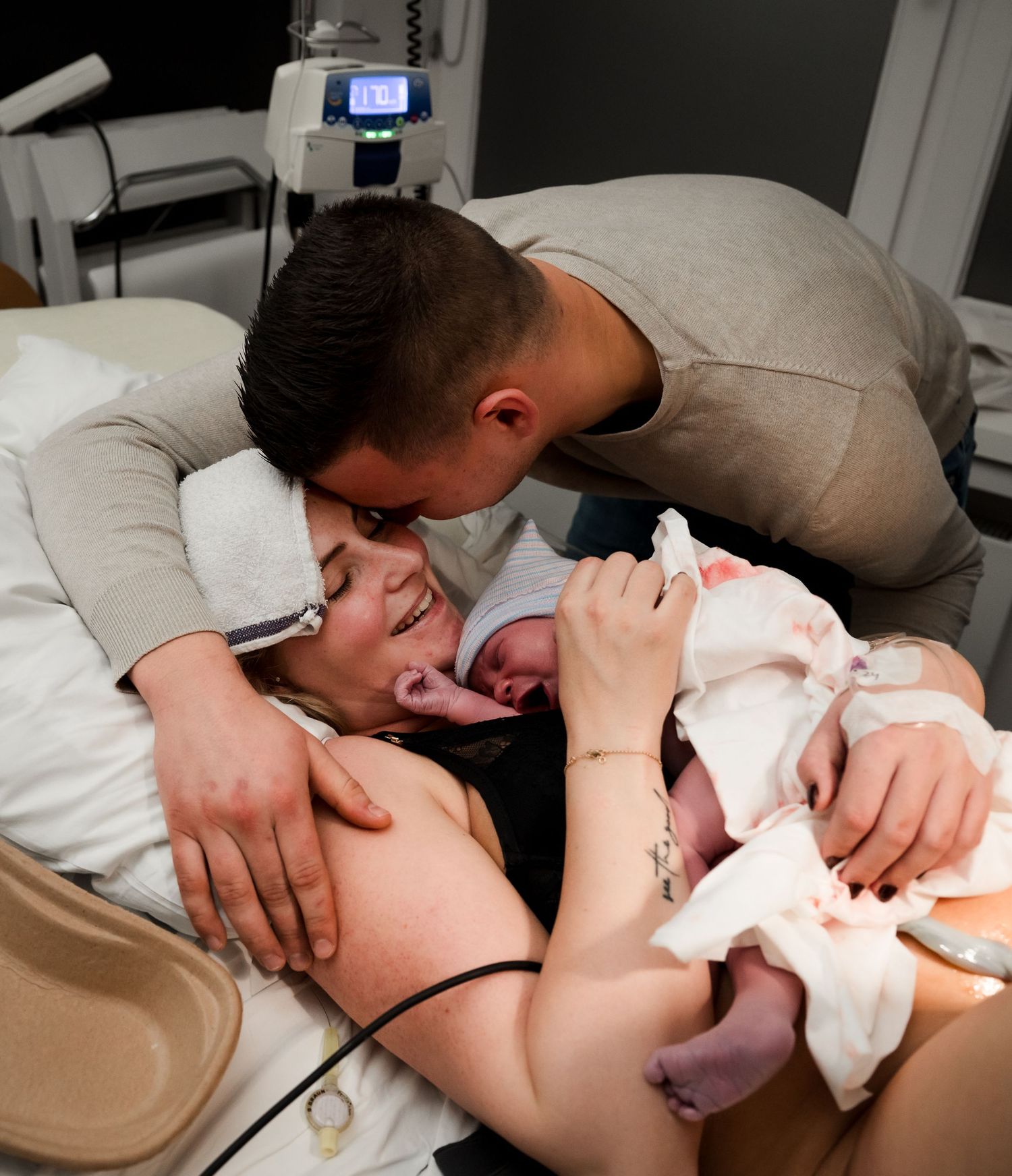 A parent gently kisses their newborn baby while being supported by nurses in a hospital delivery room.