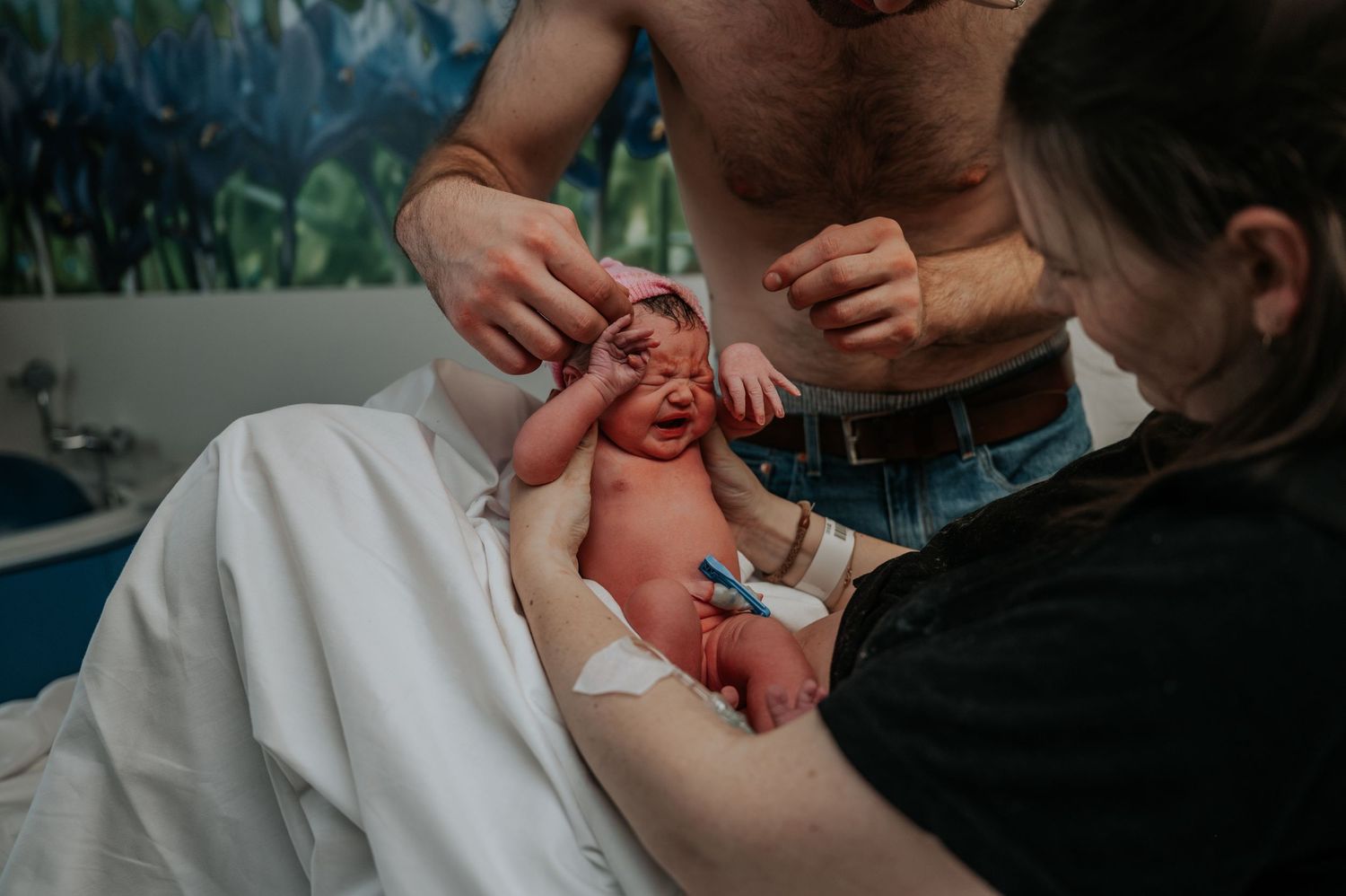 A newborn baby crying while being cradled in white fabric as healthcare providers attend to them during delivery.