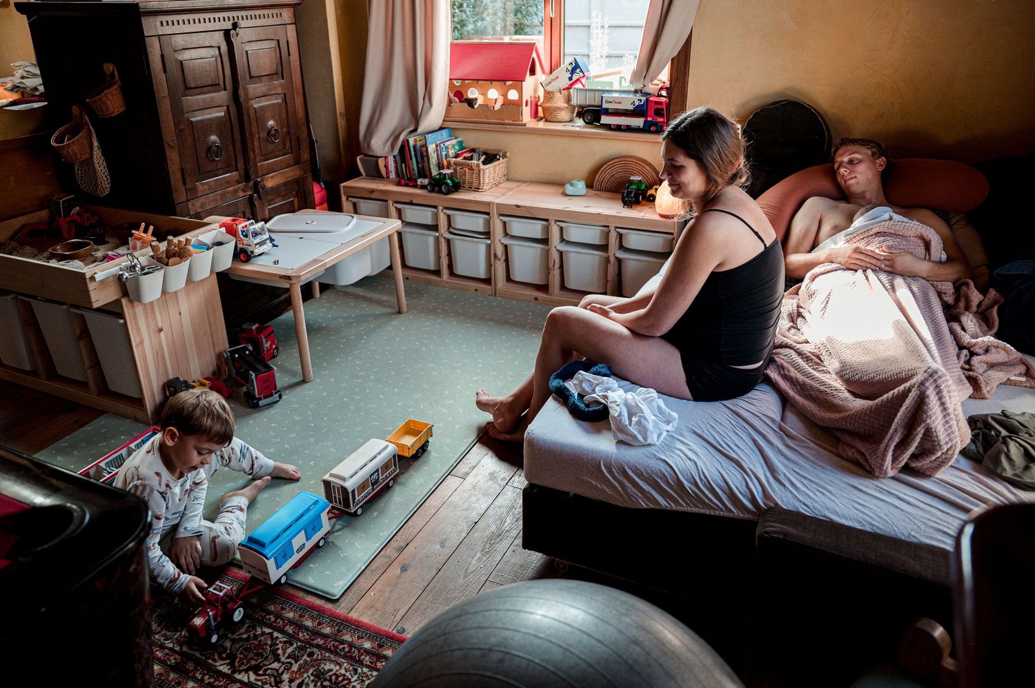 Several people sit on beds and furniture while studying in what looks like a dormitory or shared living space.