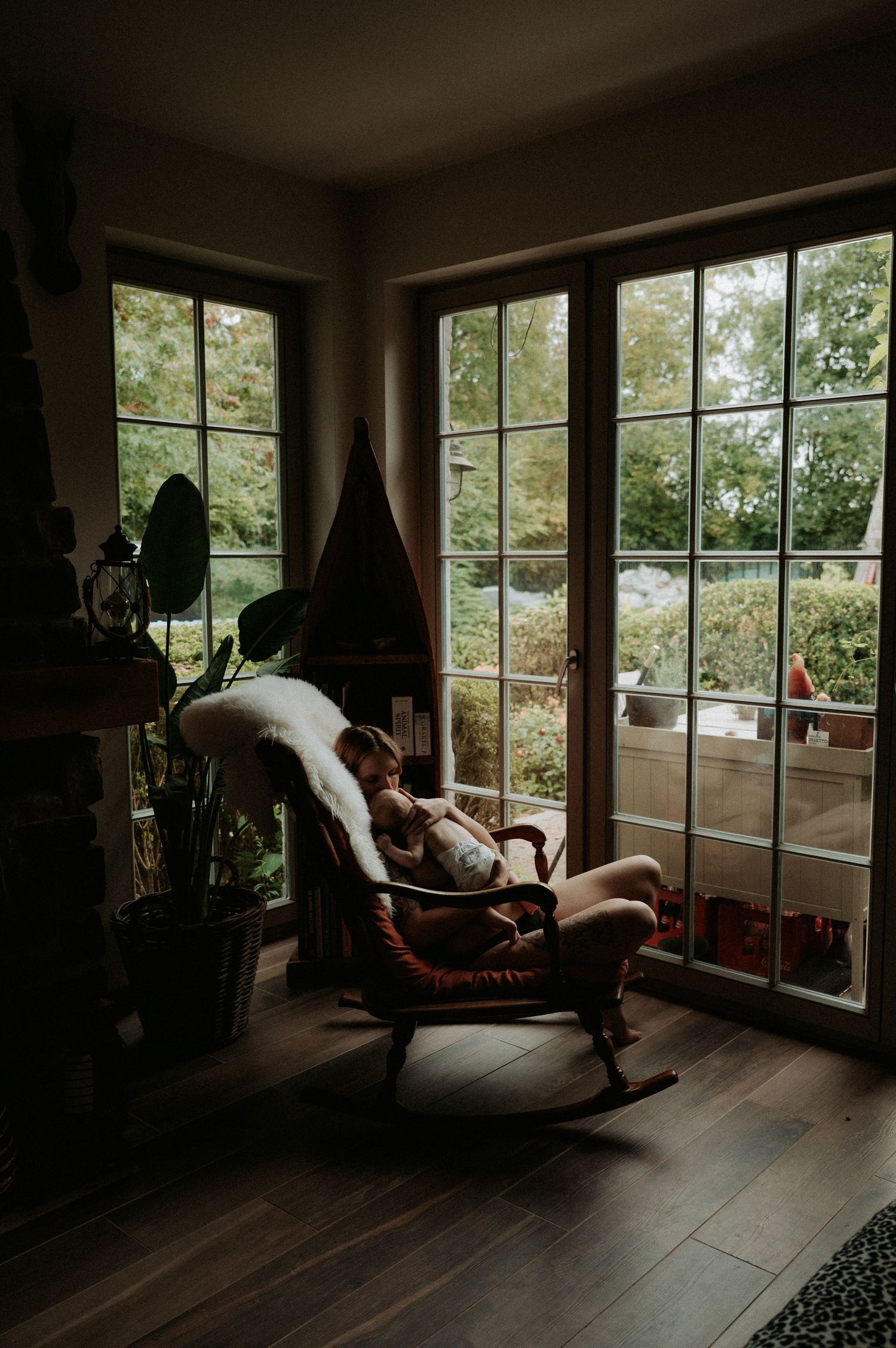 Sunlit room with people relaxing in lounge chairs by large windows overlooking greenery.