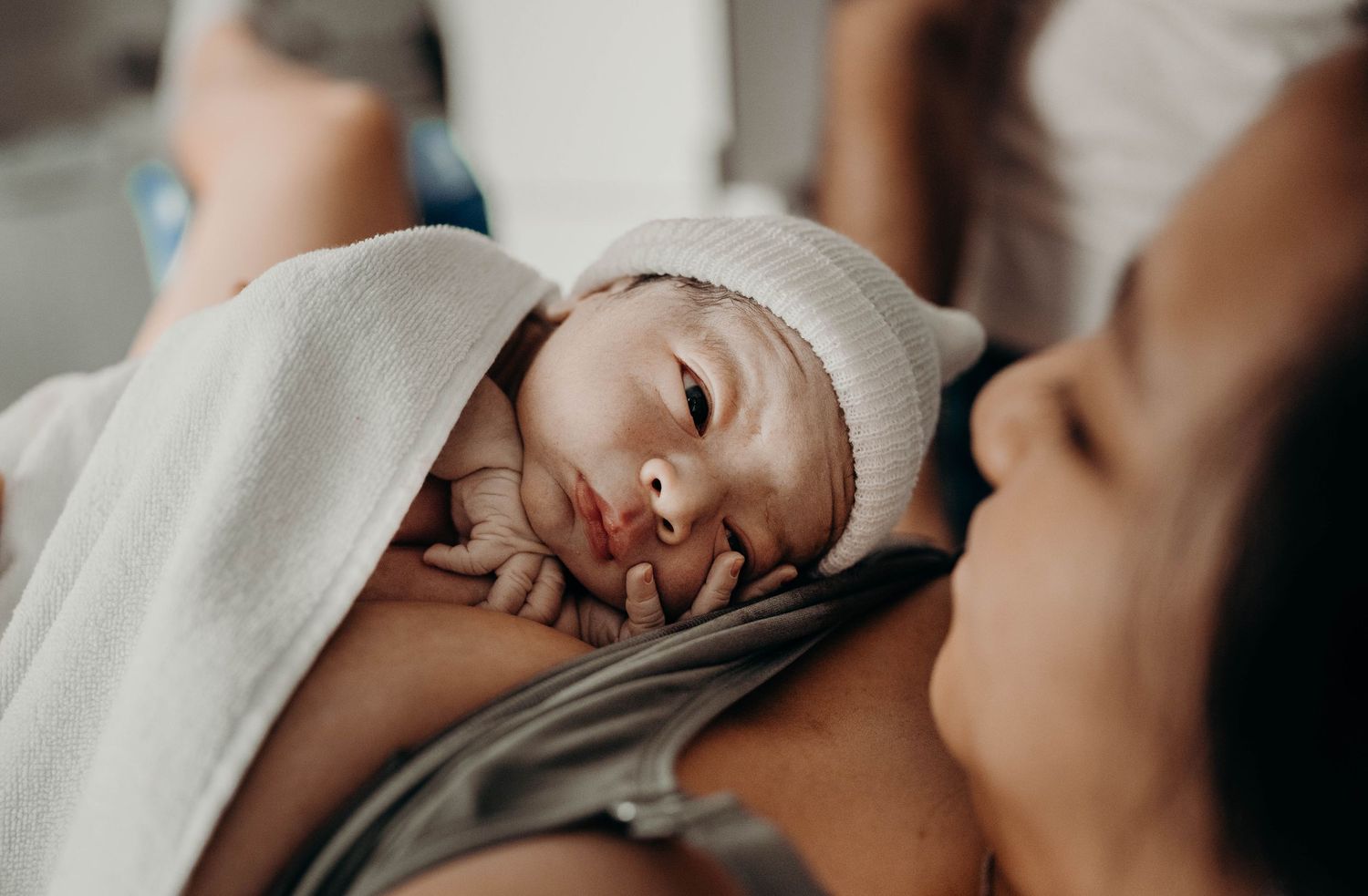 Close-up shot of newborn baby resting on parent's chest in soft lighting.