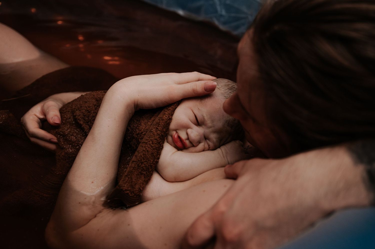 Sleeping person holding a brown blanket while laying on a dark surface in intimate low light photography.