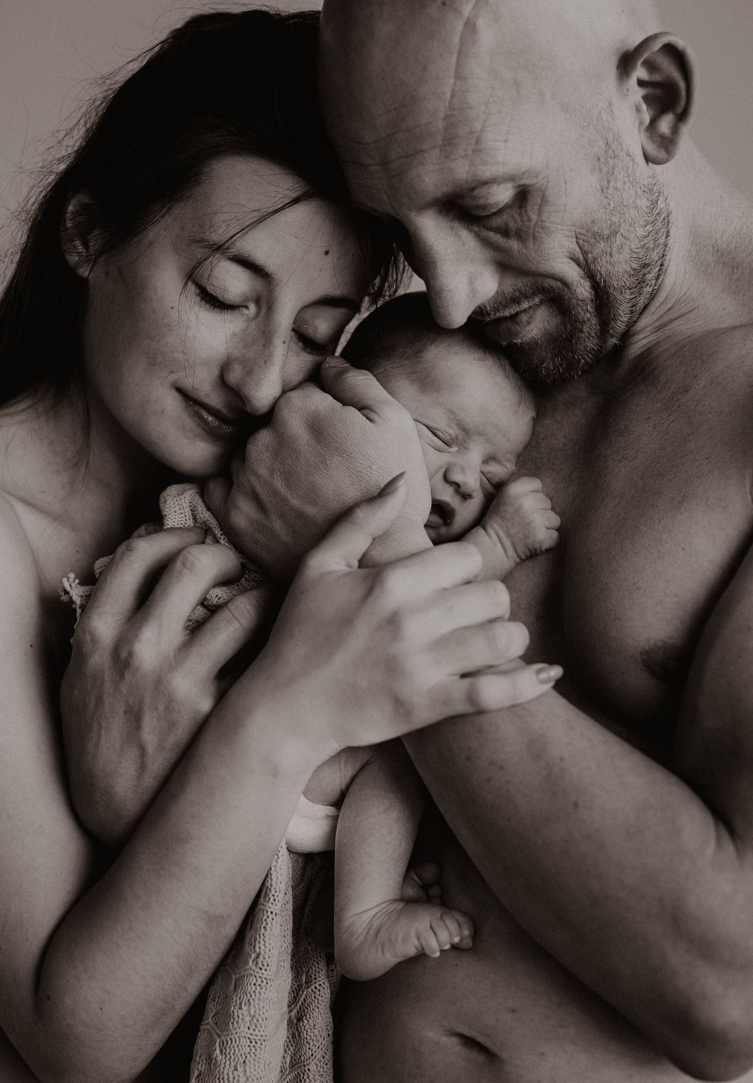 An intimate black and white portrait of a newborn being embraced by loving parents.