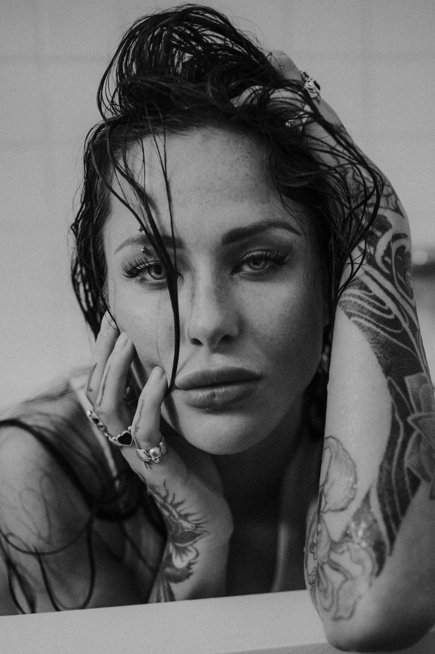 Dramatic black and white close-up portrait with wet hair and visible tattoos.