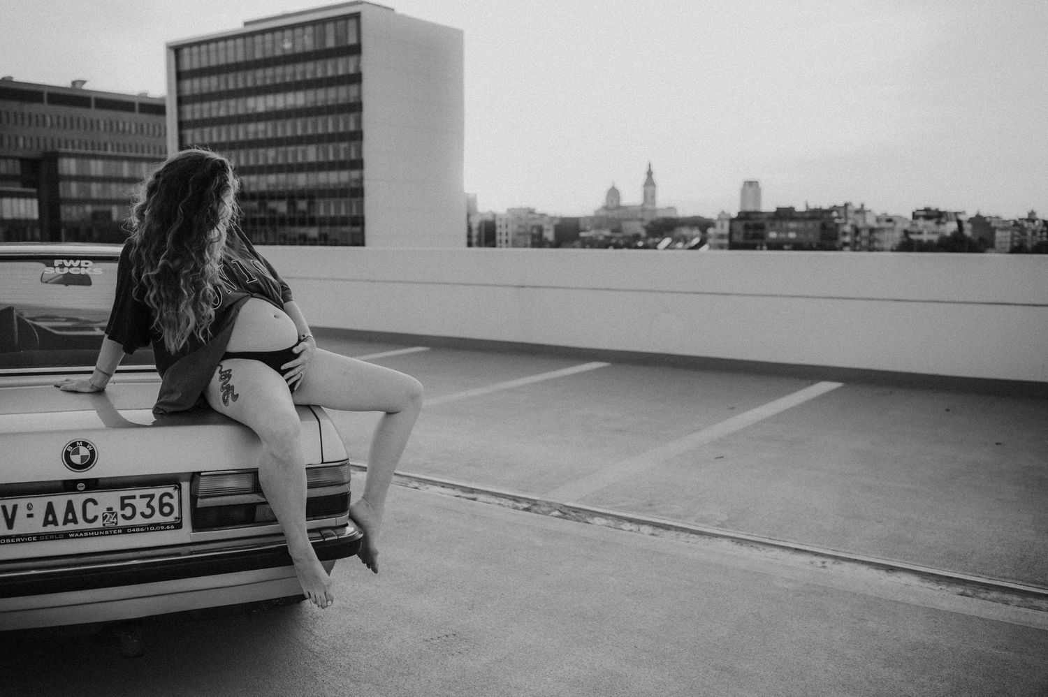 Black and white urban photo of someone sitting on a vintage BMW on a rooftop parking structure.