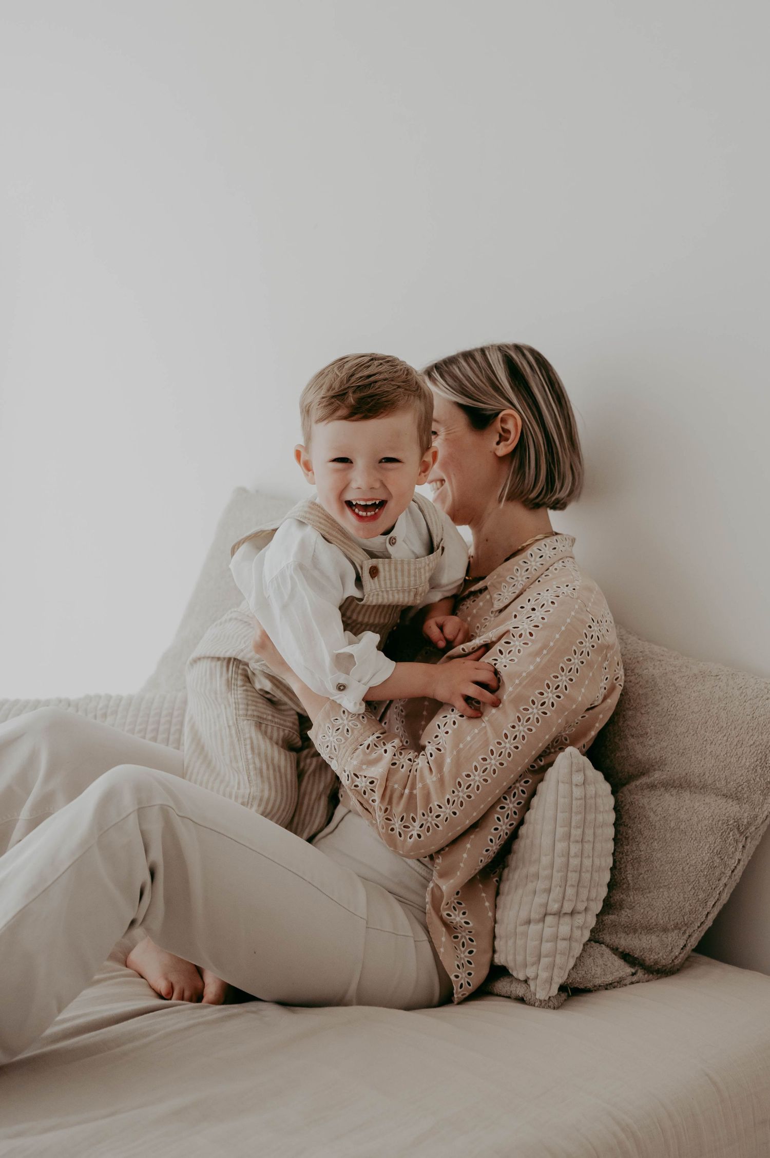 Intimate lifestyle portrait of parent and child sharing laughter on beige couch.