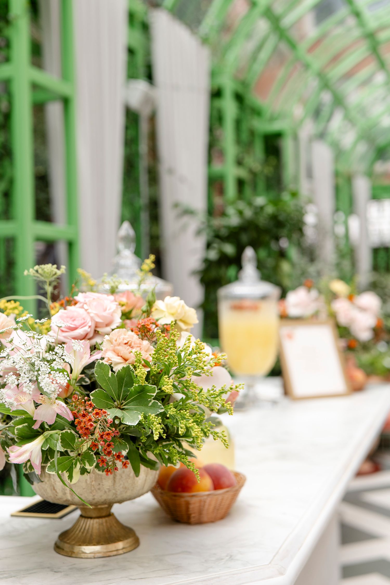 Fresh floral centerpiece with pink roses and greenery in a gold vase on white table.
