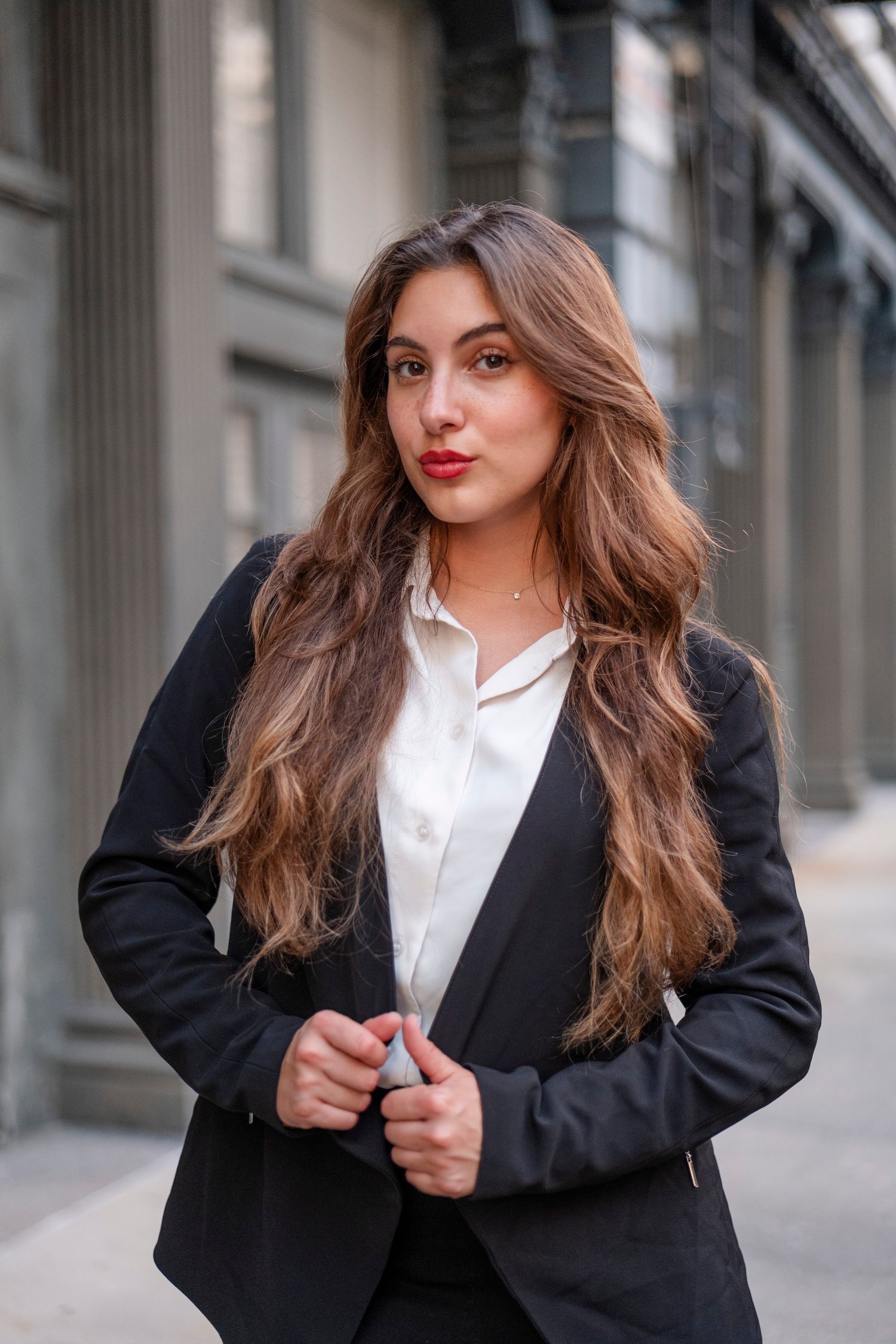 Professional in black blazer and white shirt poses against urban backdrop.