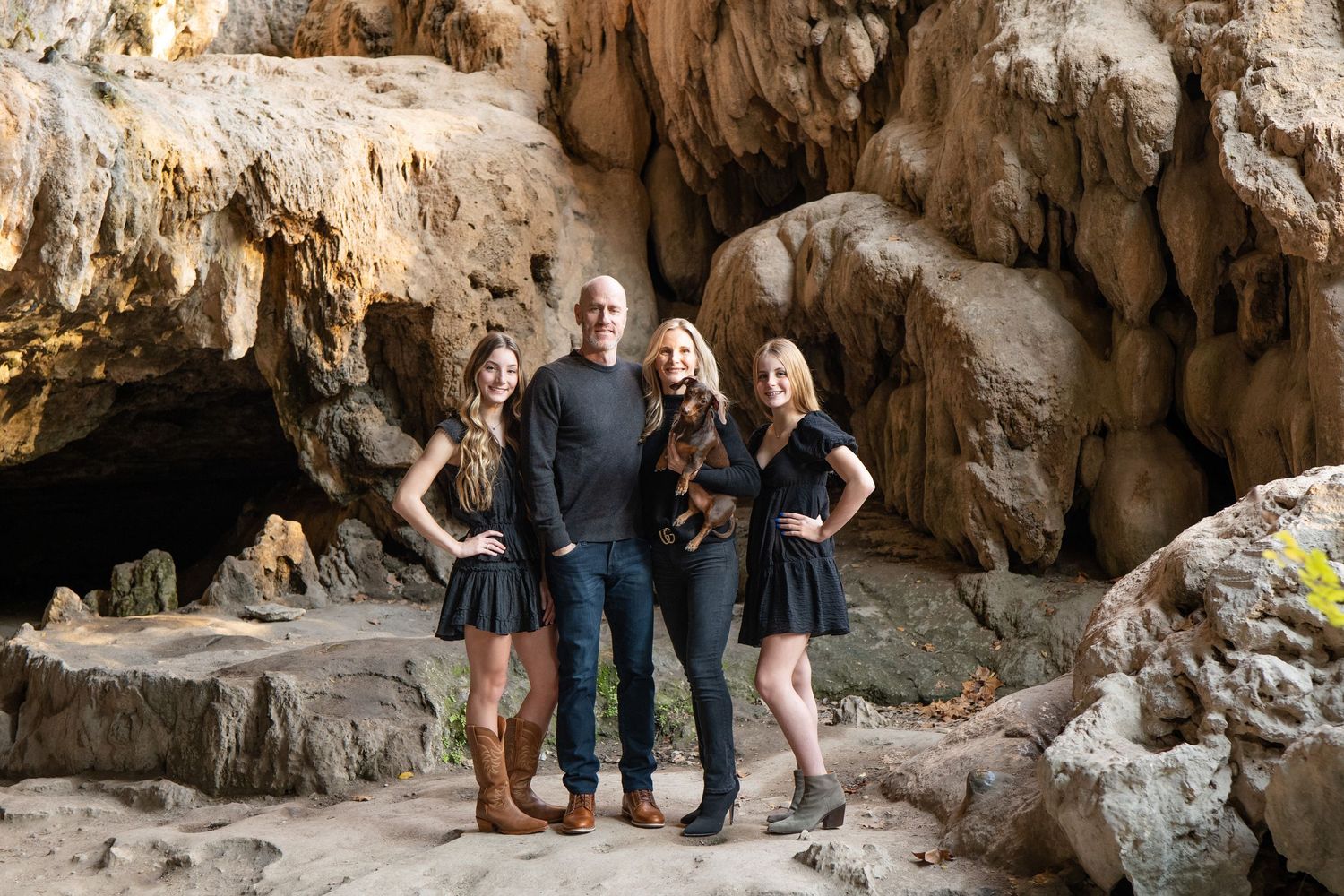 Three people pose together for a portrait in front of a rugged rock formation in natural lighting.
