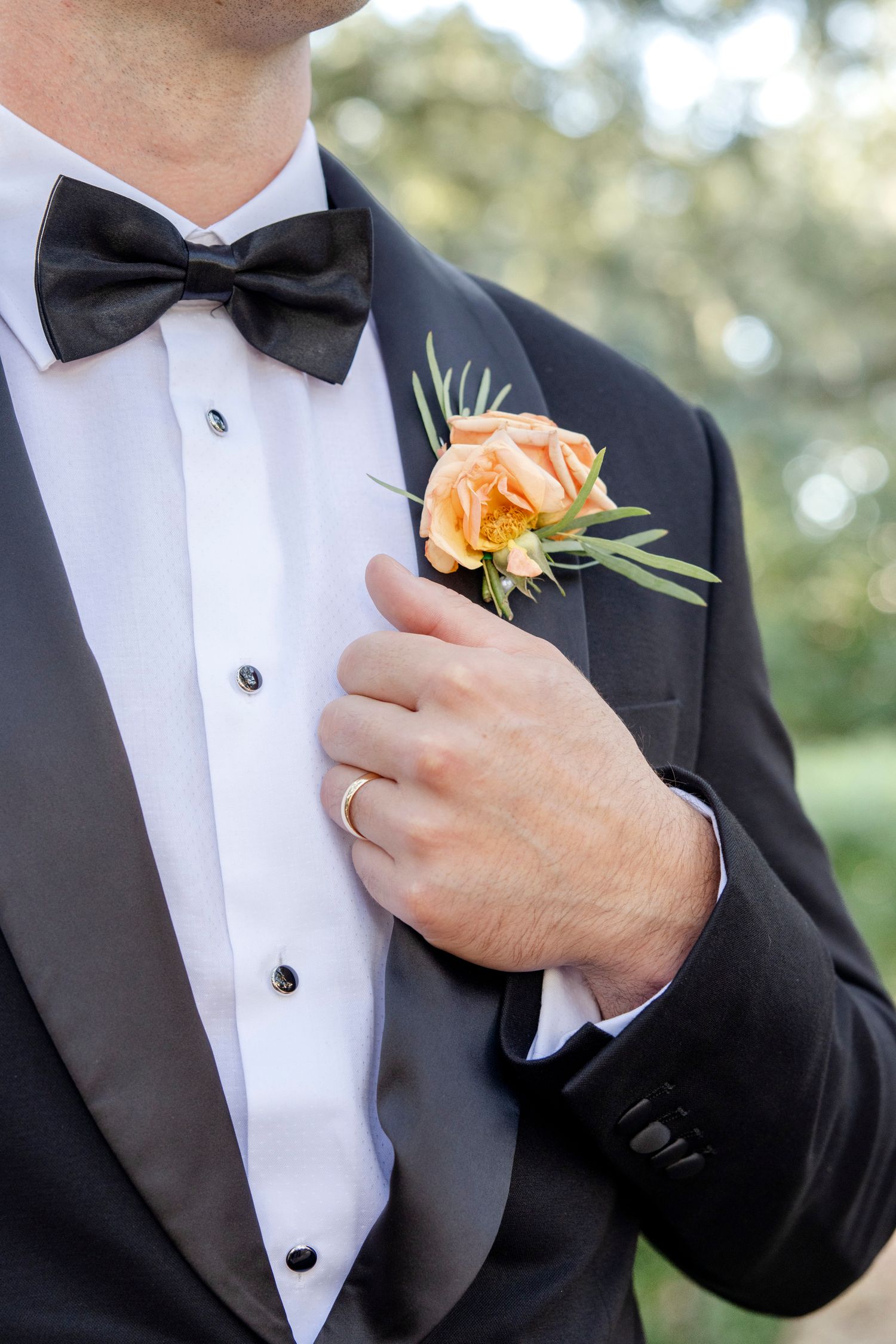 A peach rose boutonniere adorns a black tuxedo with bow tie and white dress shirt at a formal event.