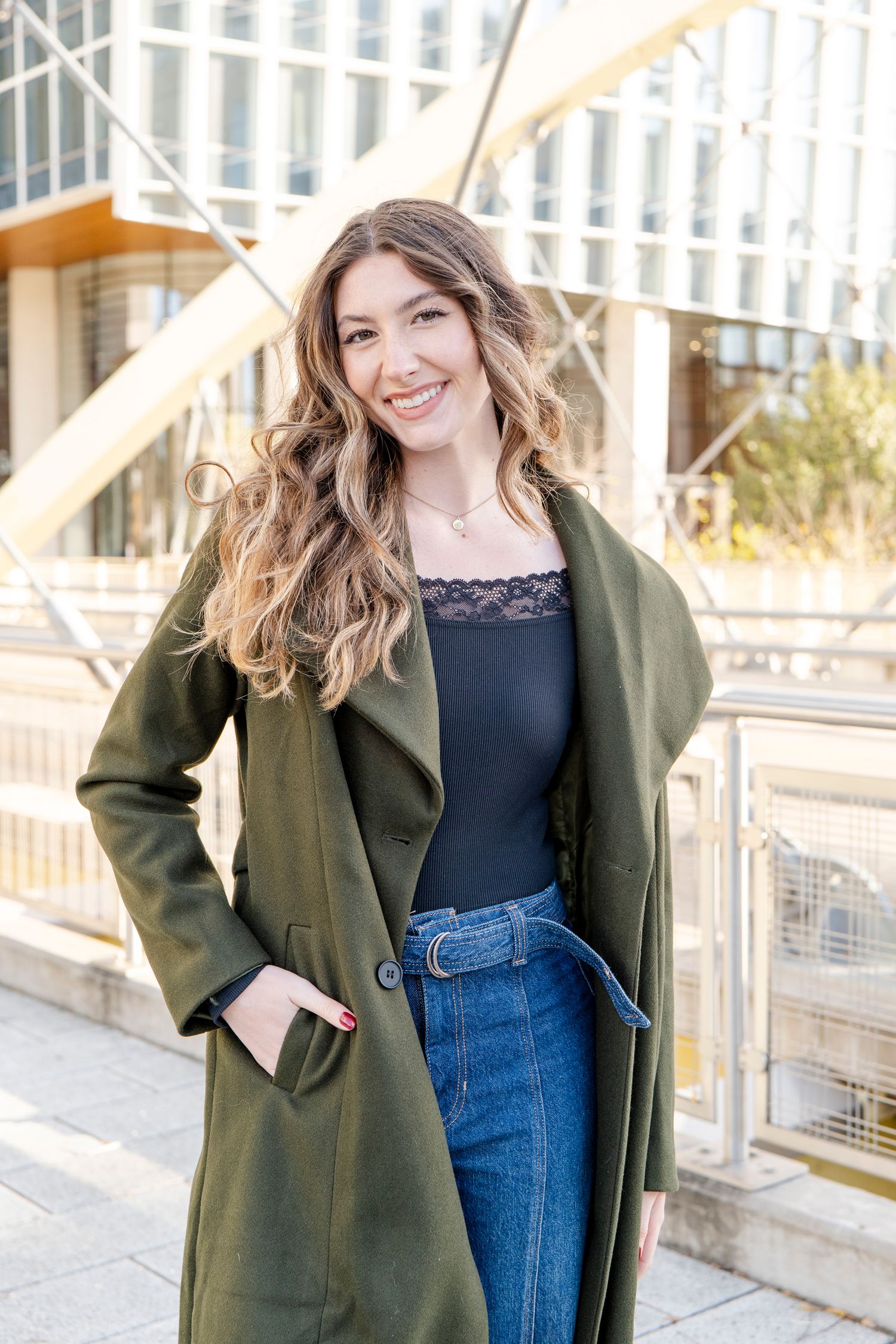 Casual portrait of person wearing olive green coat and jeans in urban setting.