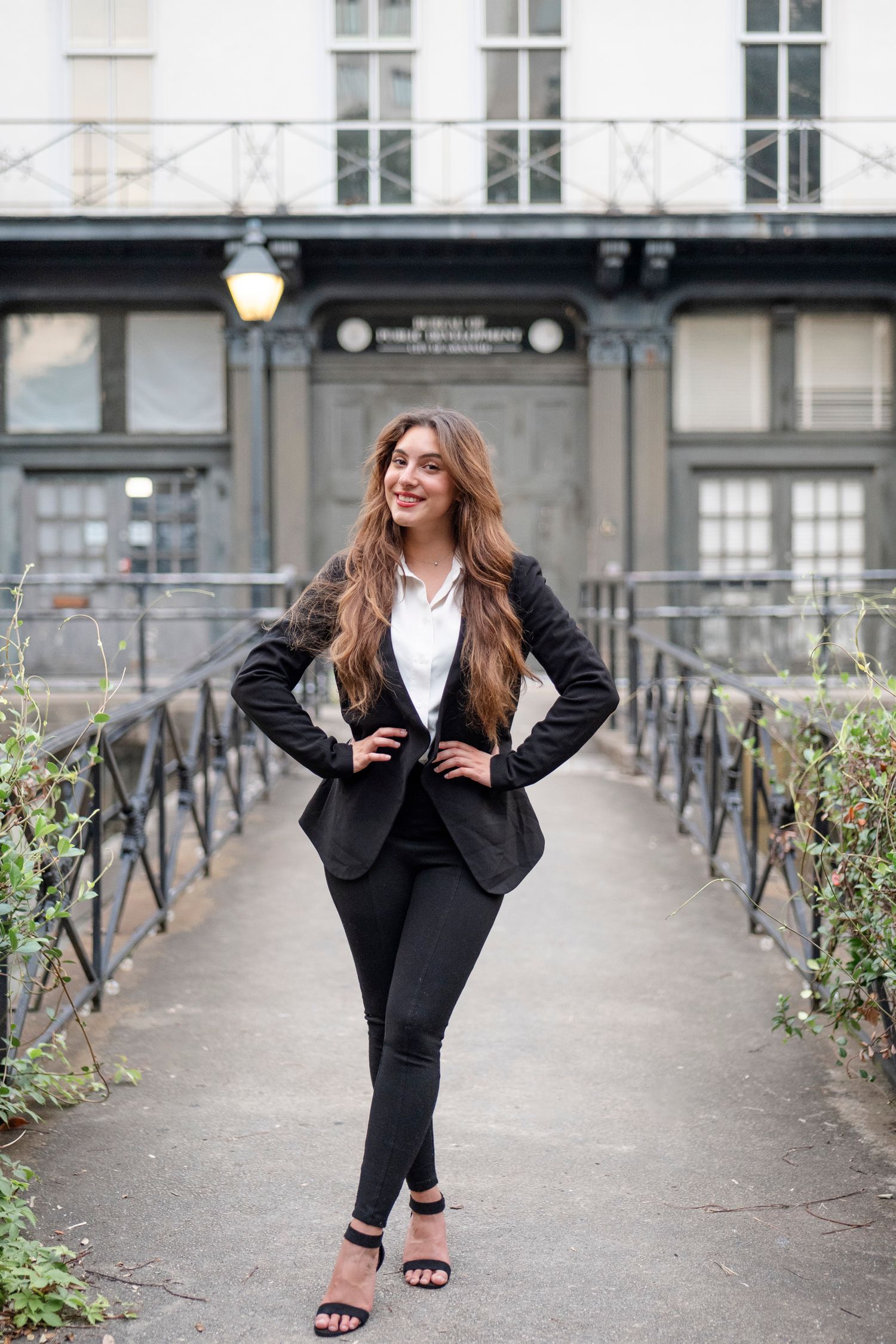 Stylish black suit look with heels on historic bridge walkway.