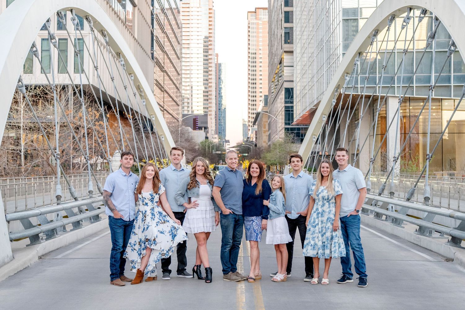 A group of people dressed in blue and white outfits pose together on a modern urban bridge with city buildings in the background.