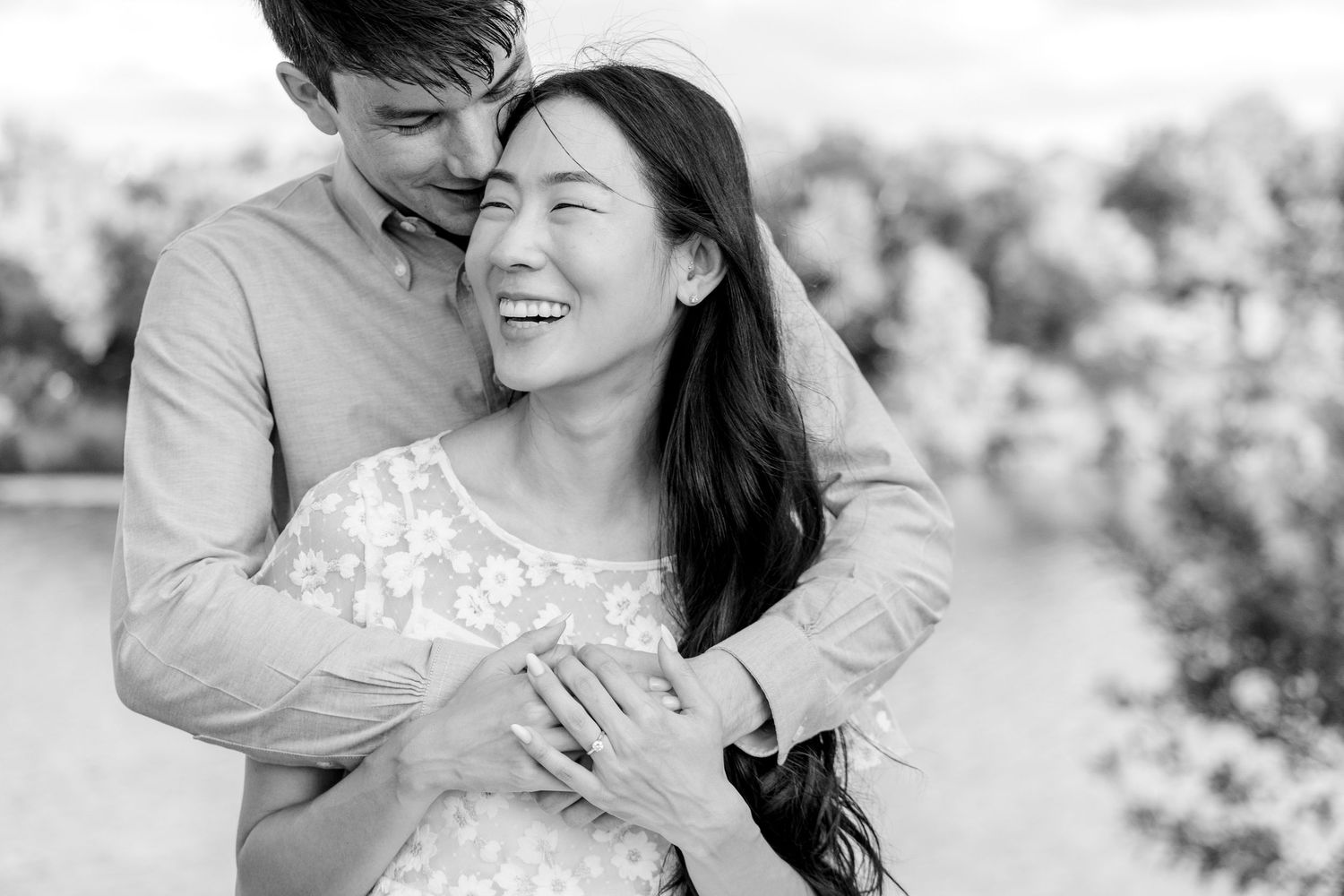 Happy couple embracing in black and white engagement photos with natural lighting outdoors.