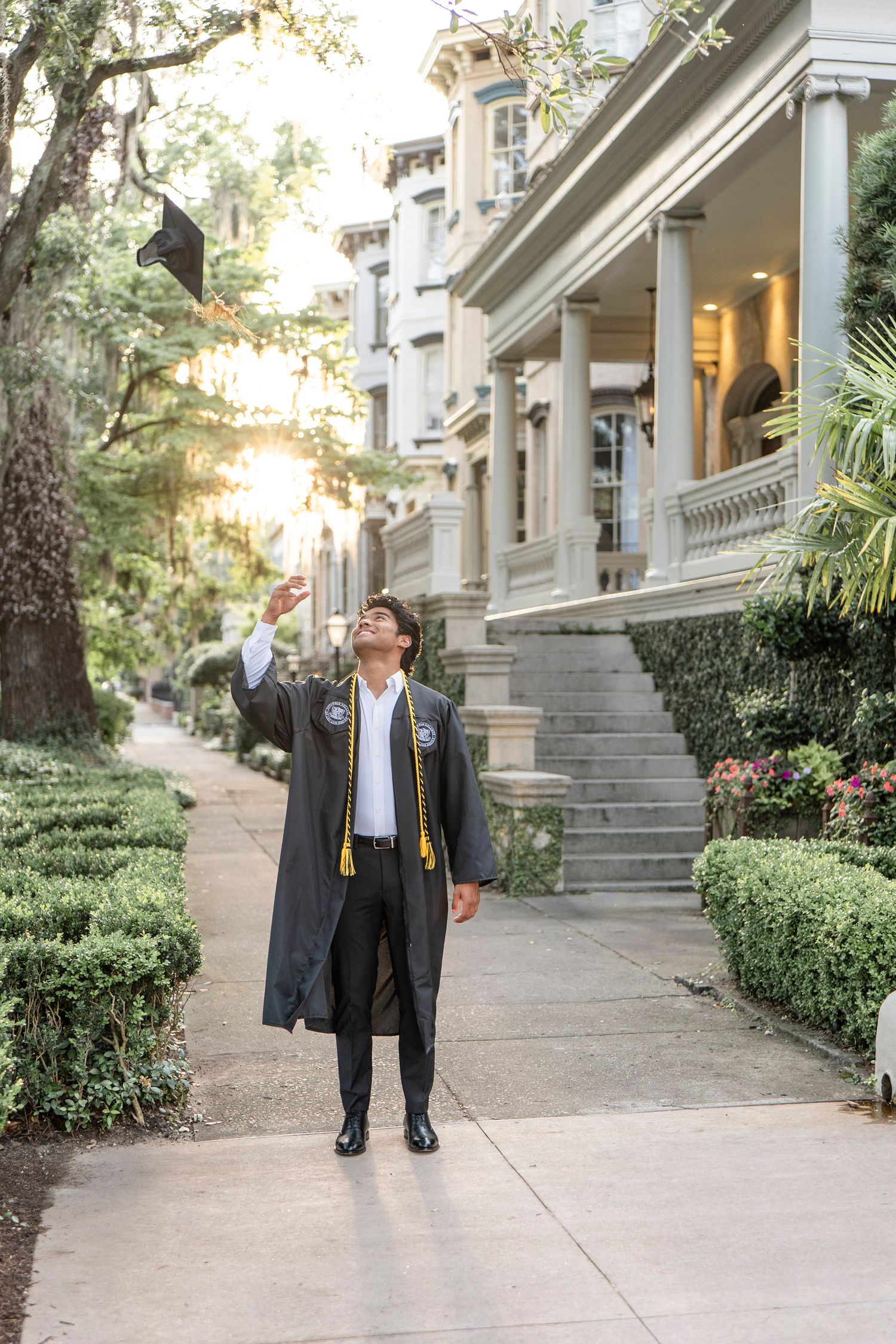 A graduate in regalia celebrating outside a grand historic building at sunset.